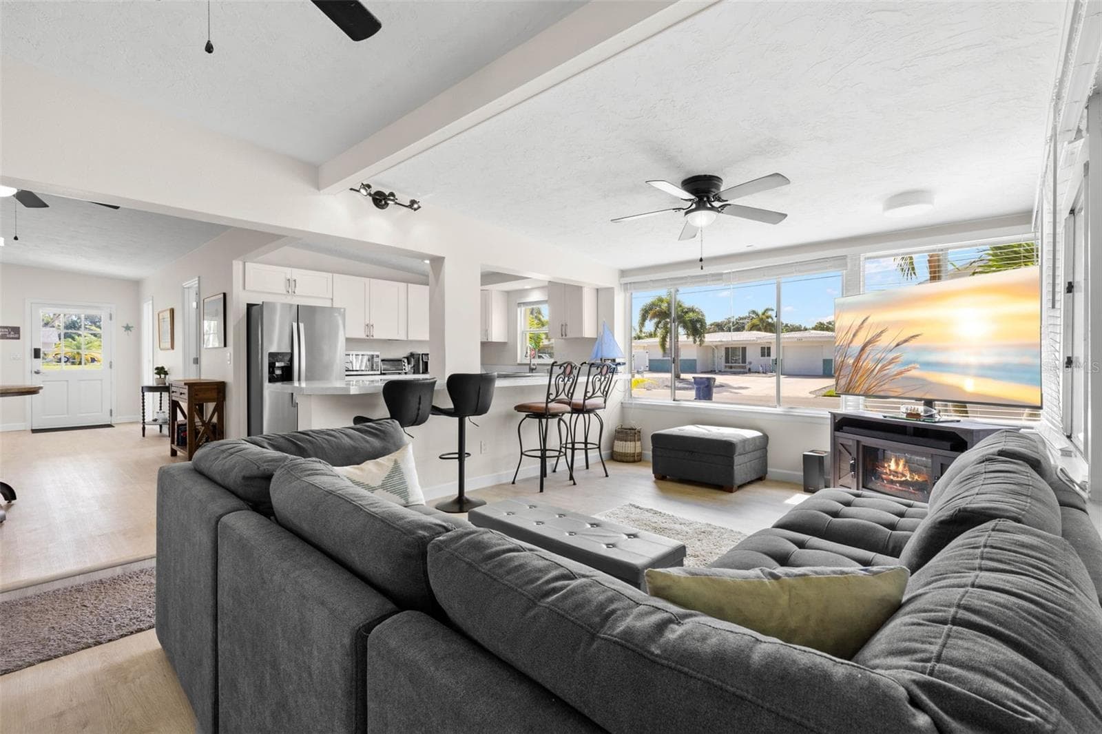 Expansive windows flood the living room with natural light, while the open connection to the updated kitchen, breakfast bar, ceiling fan, and fireplace creates a bright, comfortable gathering space. - 332 WESTWINDS DR, PALM HARBOR