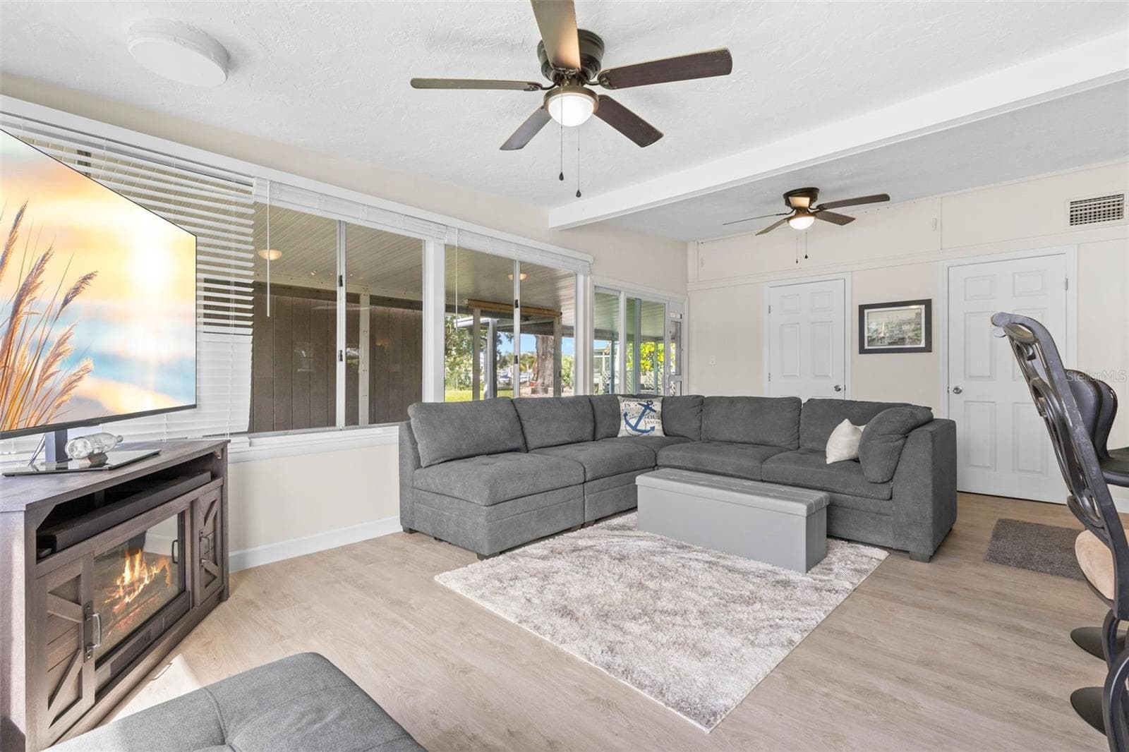 The spacious living room offers dual ceiling fans, luxury vinyl plank flooring, (2025) and a cozy fireplace, while a wall of windows and glass doors brings in abundant natural light and extends the view toward the screened porch and backyard. - 332 WESTWINDS DR, PALM HARBOR