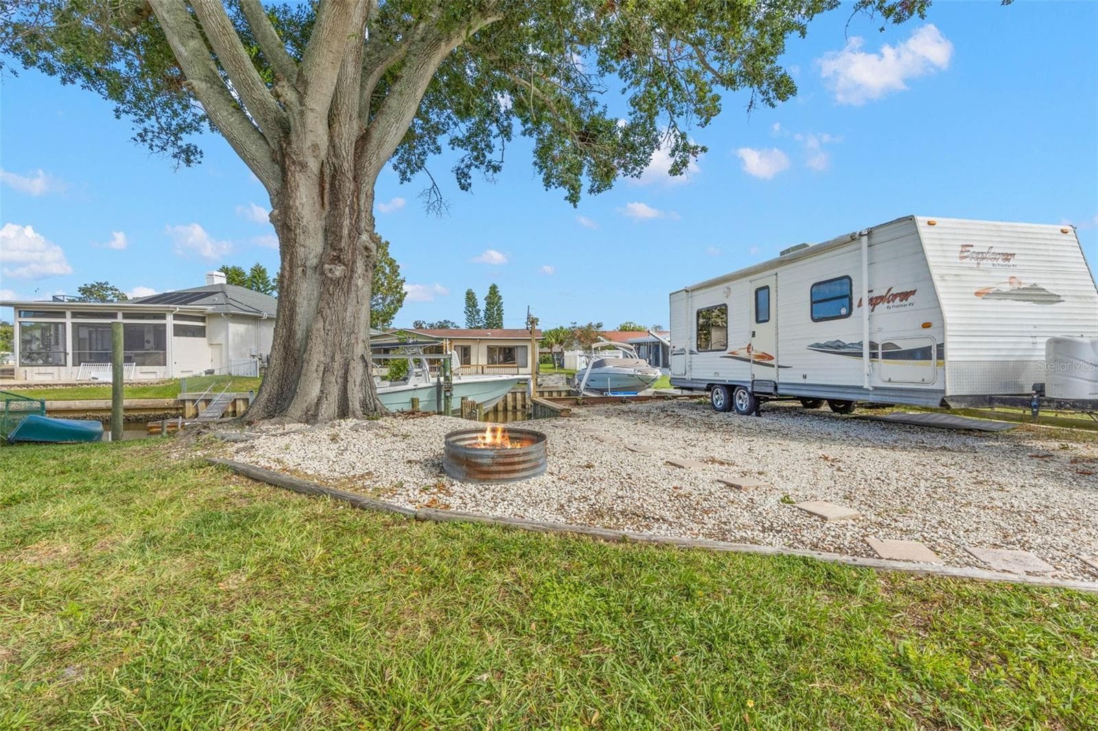 The extended side yard adds exceptional flexibility with room for RV, boat, or trailer parking, while a gravel gathering area with a fire pit sits beneath a massive shade tree just steps from the canal. - 332 WESTWINDS DR, PALM HARBOR