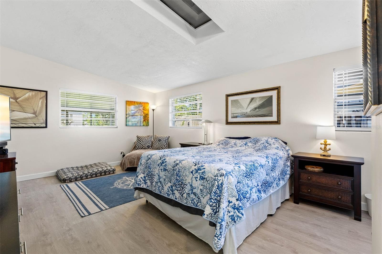 The generously sized primary bedroom feels bright and airy with multiple windows, a skylight overhead, neutral tones, and luxury vinyl plank flooring (2025), plus plenty of room for a sitting area in addition to a king-size bed. - 332 WESTWINDS DR, PALM HARBOR