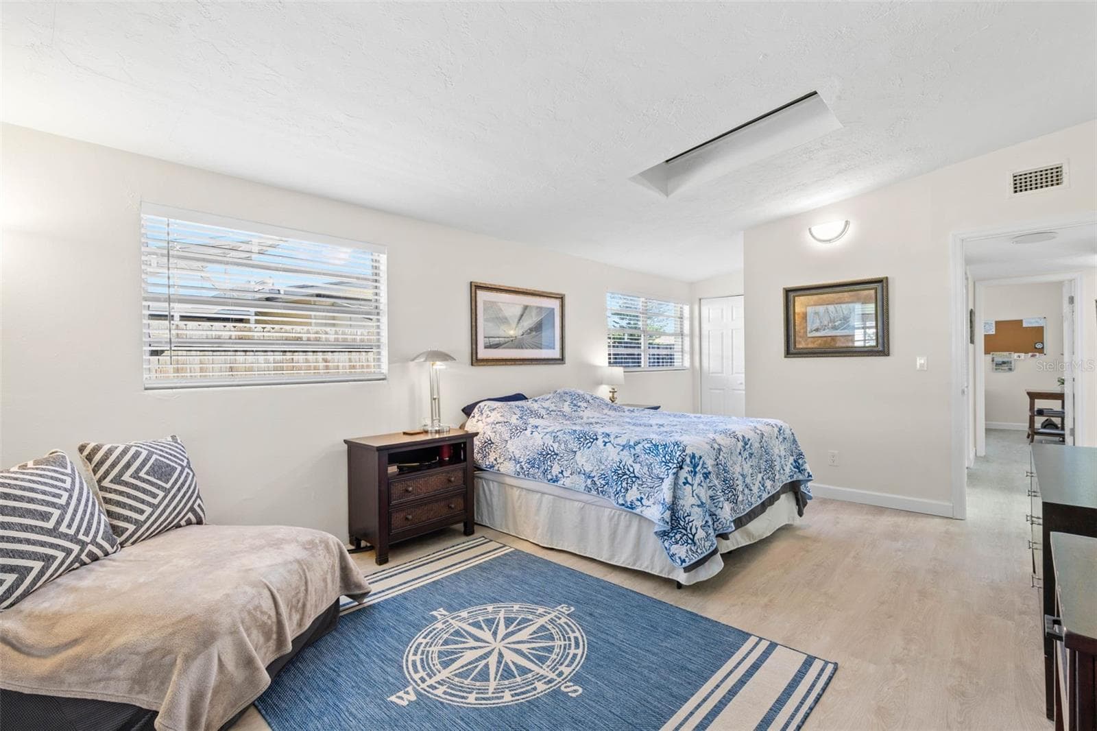 The spacious primary bedroom easily accommodates a king-size bed and a dedicated sitting area, with multiple windows, a skylight, neutral tones, and luxury vinyl plank flooring (2025) adding to the bright, open feel. - 332 WESTWINDS DR, PALM HARBOR