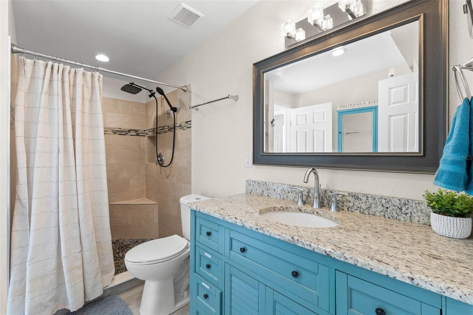 The updated second bath features a turquoise vanity with granite countertop, framed mirror, modern lighting, and a tiled walk-in shower with built-in bench, rainfall showerhead, and handheld sprayer. - 332 WESTWINDS DR, PALM HARBOR