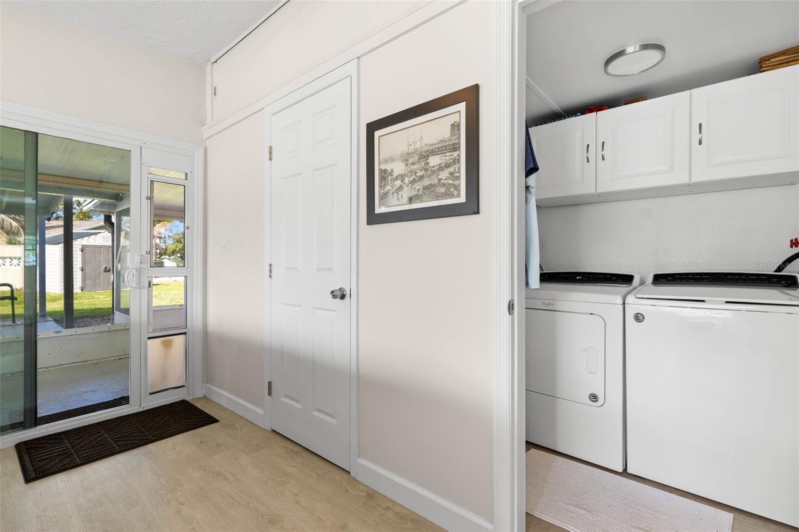 A dedicated laundry room keeps everyday chores tucked neatly away, with a full-size washer and dryer, overhead cabinetry for storage, and convenient access to the screened lanai and backyard. - 332 WESTWINDS DR, PALM HARBOR