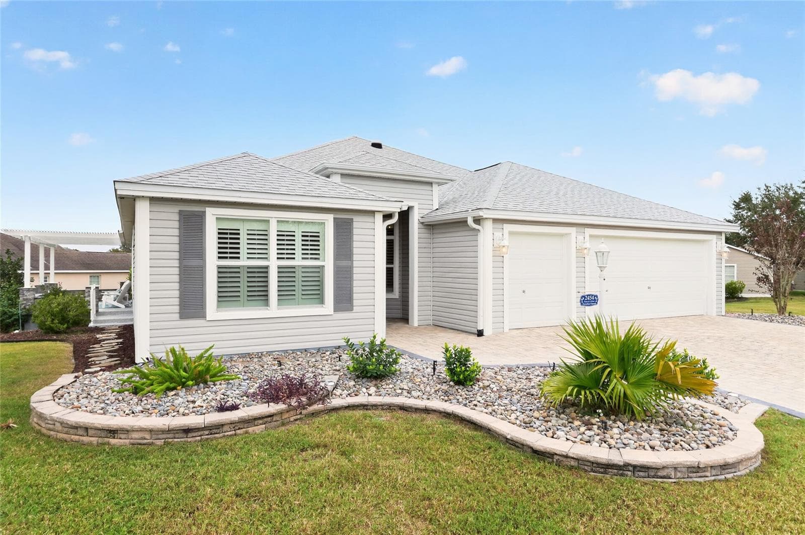 Beautifully tiered landscaping with decorative stone and tropical plantings complements the paver driveway and two-car plus golf cart garage, creating a welcoming first impression. - 2454 MORNING DOVE LN, THE VILLAGES