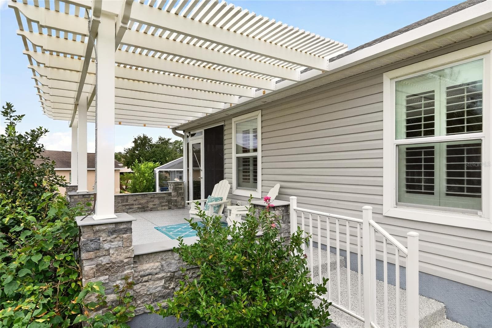 Unwind beneath the PERGOLA on this inviting patio, where decorative STONE ACCENTS and lush landscaping create a charming setting for outdoor dining and sunset conversations. - 2454 MORNING DOVE LN, THE VILLAGES