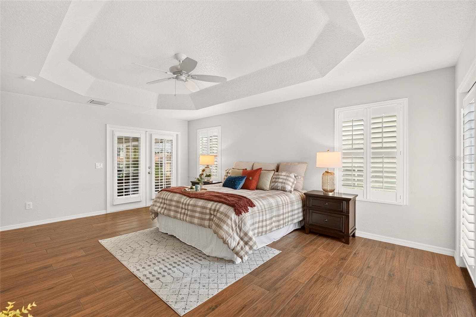 An elegant TRAY CEILING and beautiful natural light enhance this inviting PRIMARY SUITE, with French doors opening to the enclosed lanai for a peaceful place to unwind. - 2454 MORNING DOVE LN, THE VILLAGES
