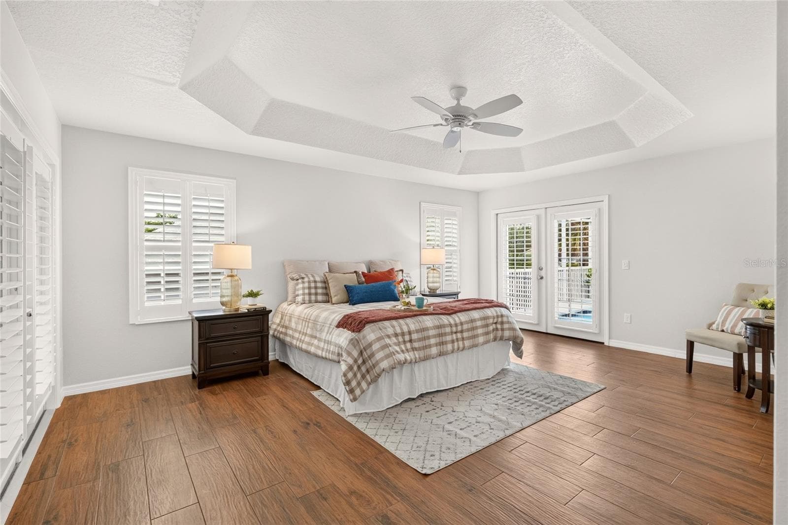 The spacious PRIMARY SUITE features an elegant TRAY CEILING, PLANTATION SHUTTERS, and French doors leading to the pool for a refreshing start or relaxing end to your day. - 2454 MORNING DOVE LN, THE VILLAGES