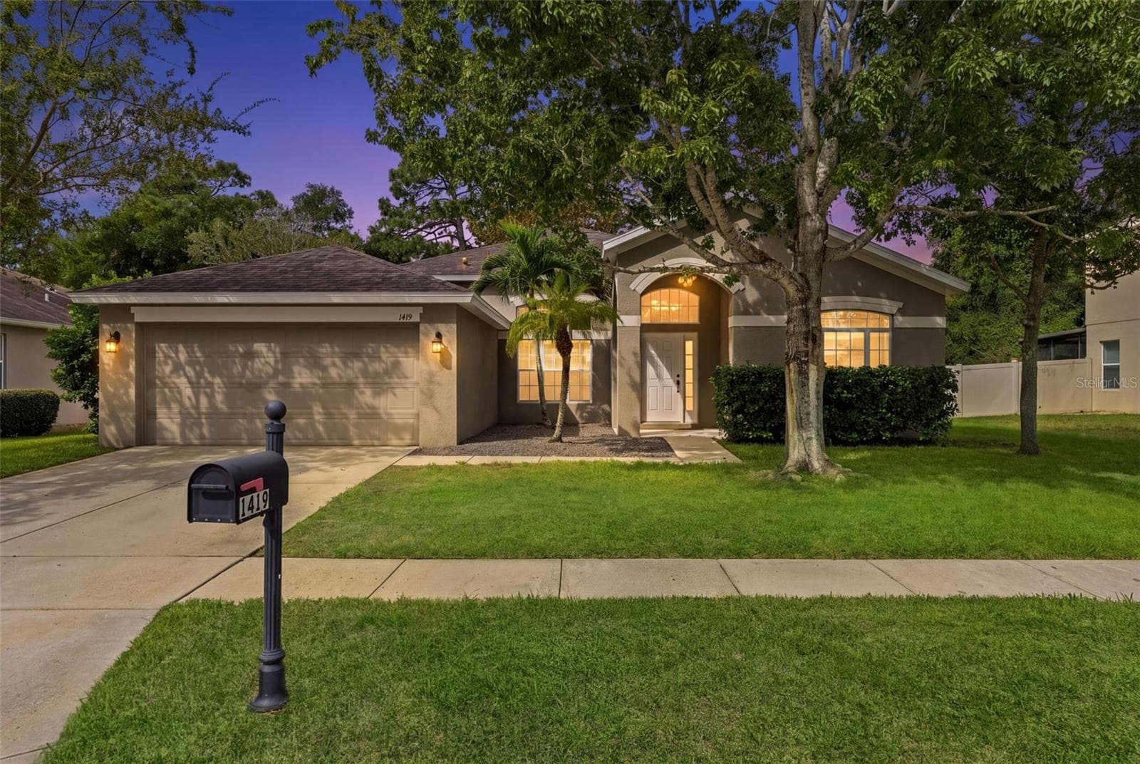 A warm twilight view highlights the home’s inviting entry and established neighborhood setting. - 1419 BLUE MARLIN BLVD, HOLIDAY