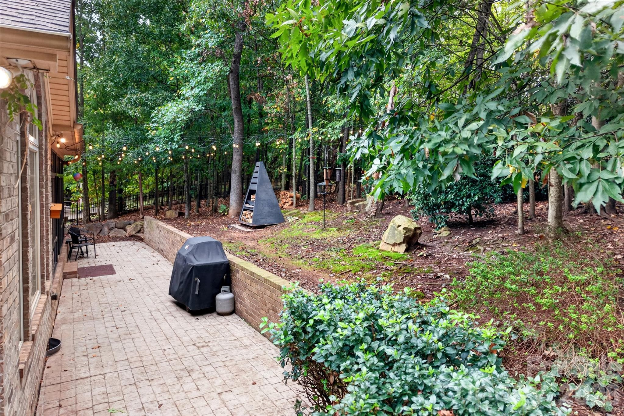 Wooded backyard with firepit that conveys and string lighting. - 3941 Grovesner Street, Harrisburg