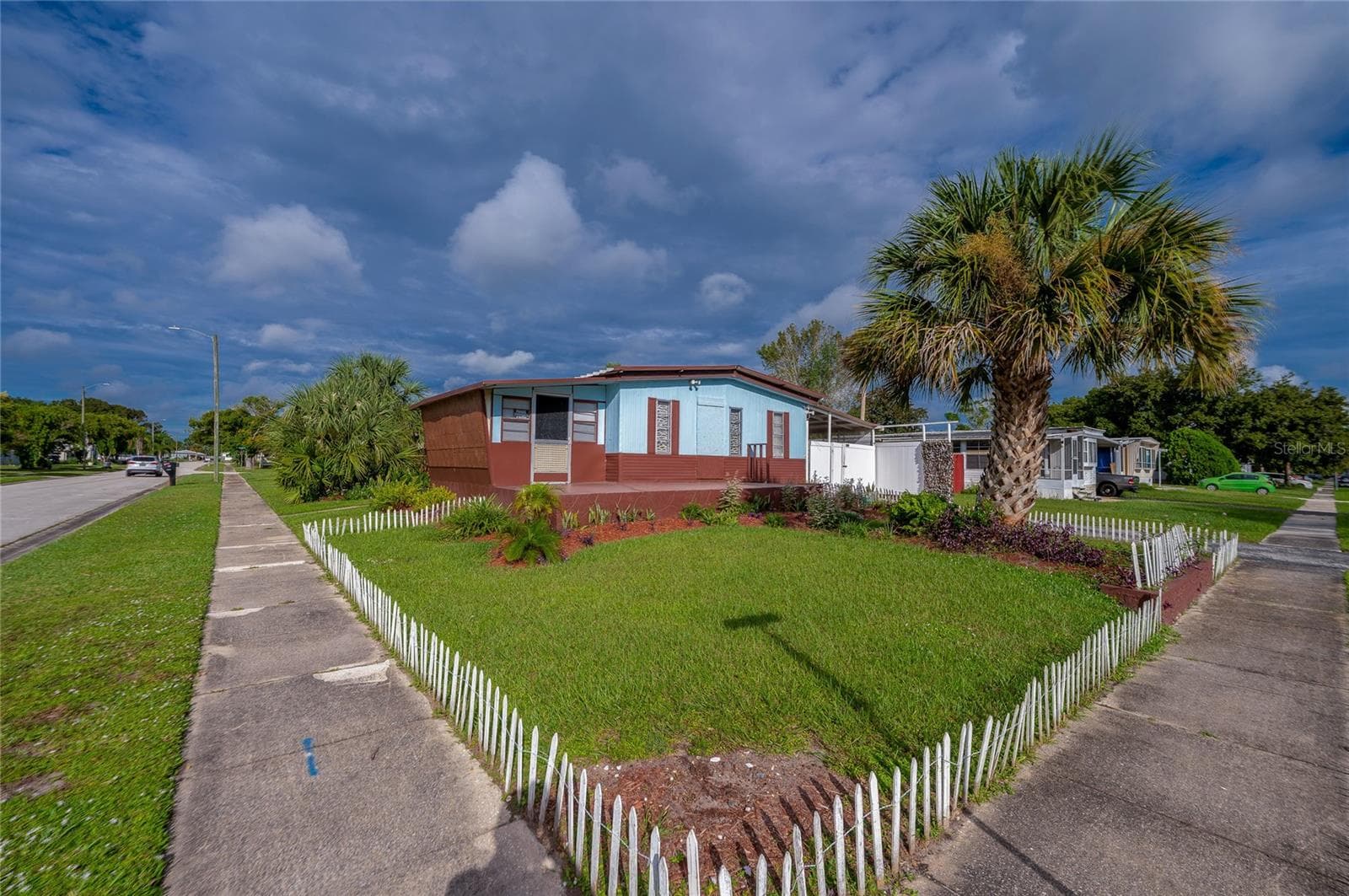 Wide exterior view highlights the corner setting, lawn, tropical landscaping, and low decorative fencing surrounding the front yard. - 128 KON TIKI TER, PORT ORANGE