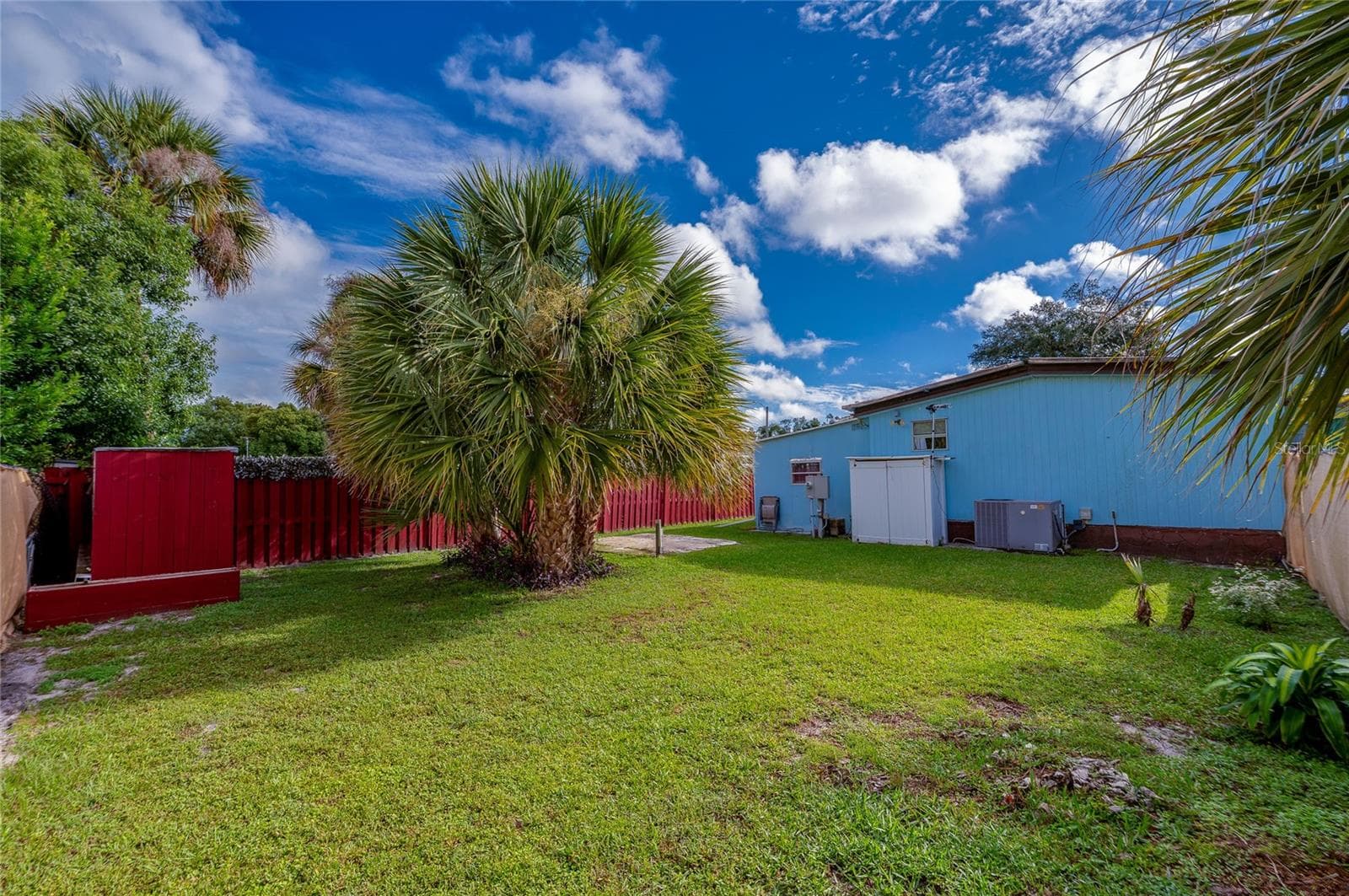 Rear view highlights the generous lawn, established tropical landscaping, and exterior access along the back of the home. - 128 KON TIKI TER, PORT ORANGE