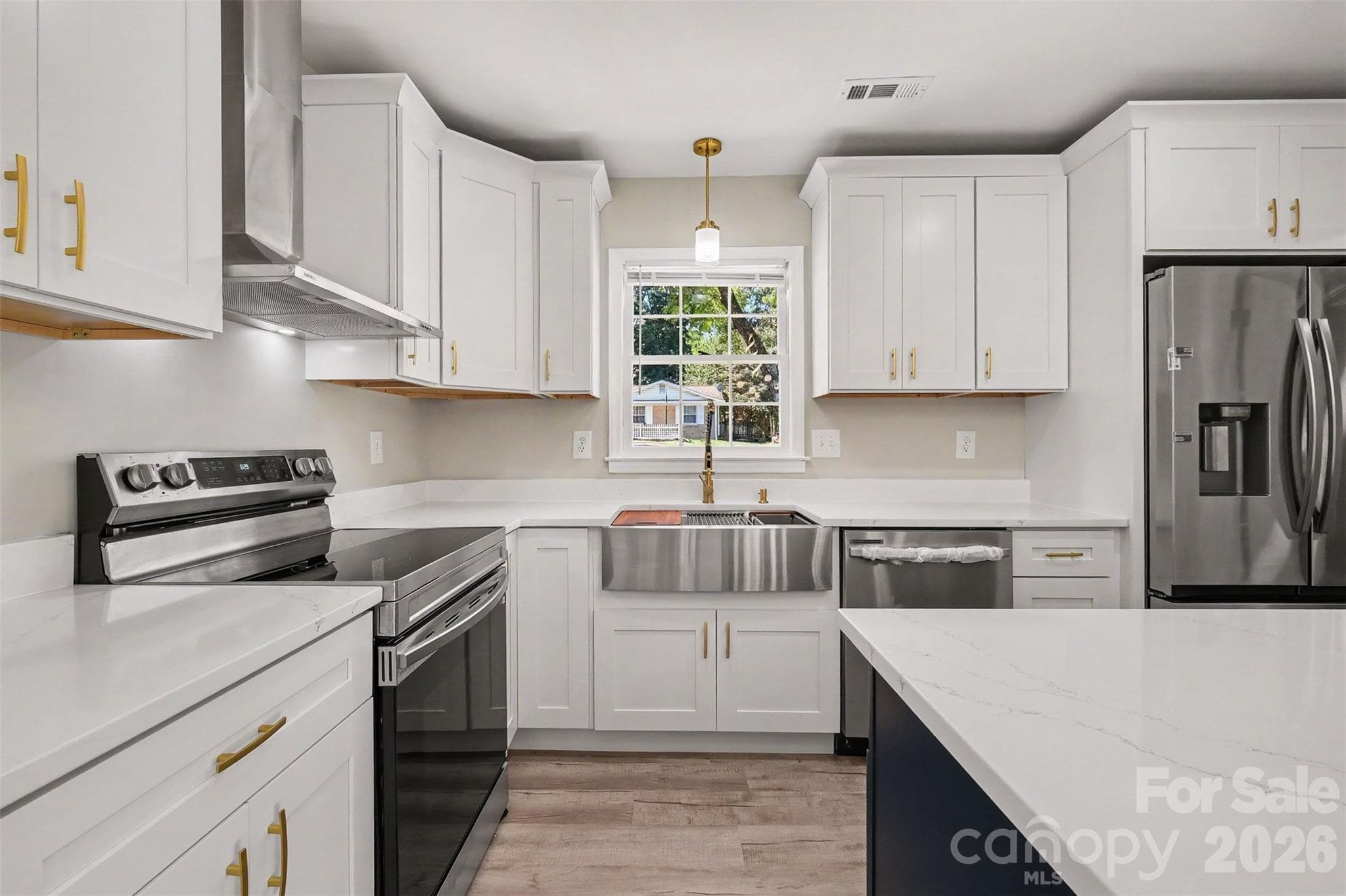 Renovated kitchen detail highlighting the stainless steel apron sink, premium range, and new white cabinetry with gold hardware. - 3801 Hillock Court, Charlotte