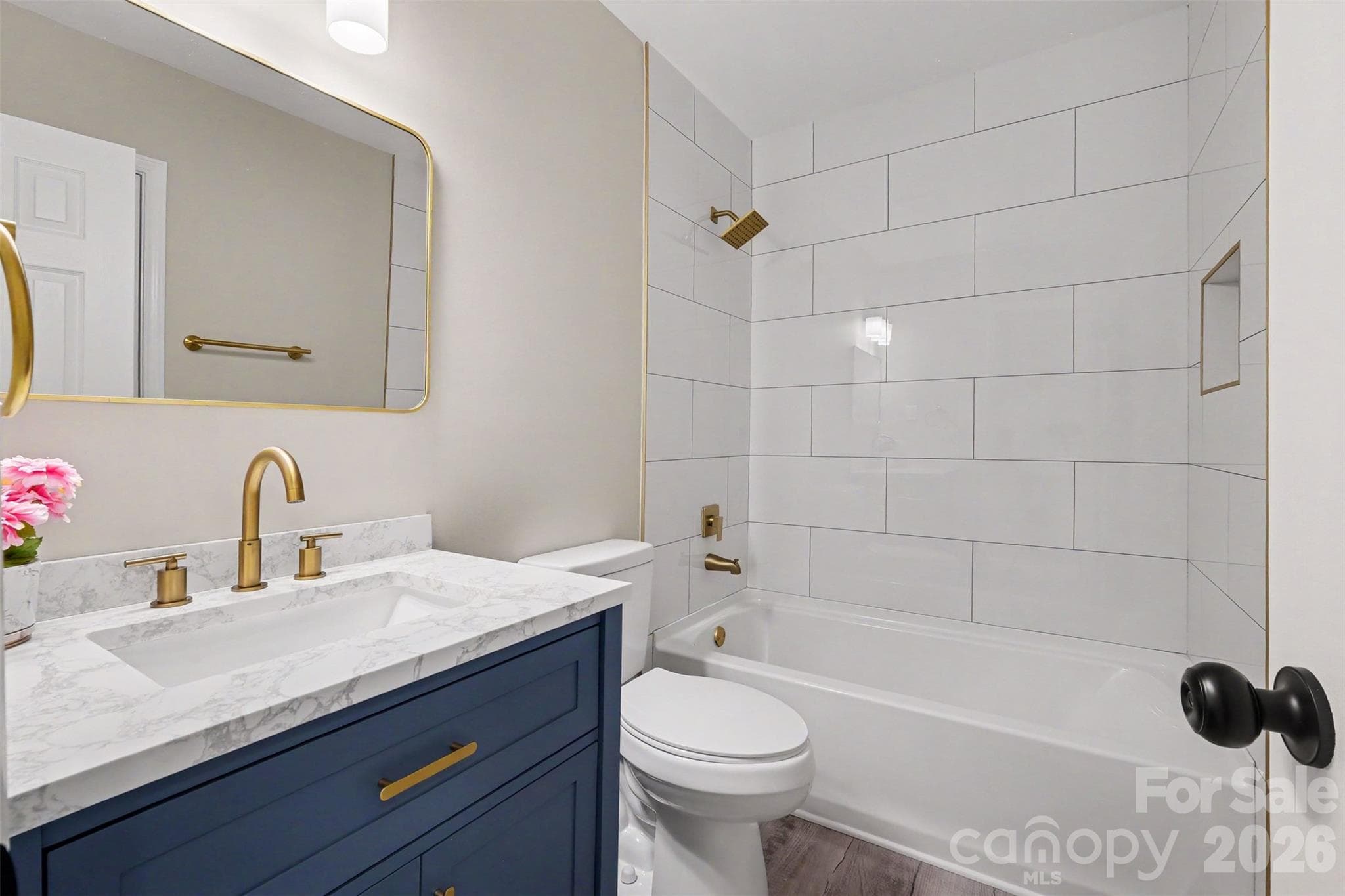 Renovated secondary bathroom featuring a navy vanity with gold hardware, updated mirror and lighting, and a custom tiled tub/shower surround. - 3801 Hillock Court, Charlotte