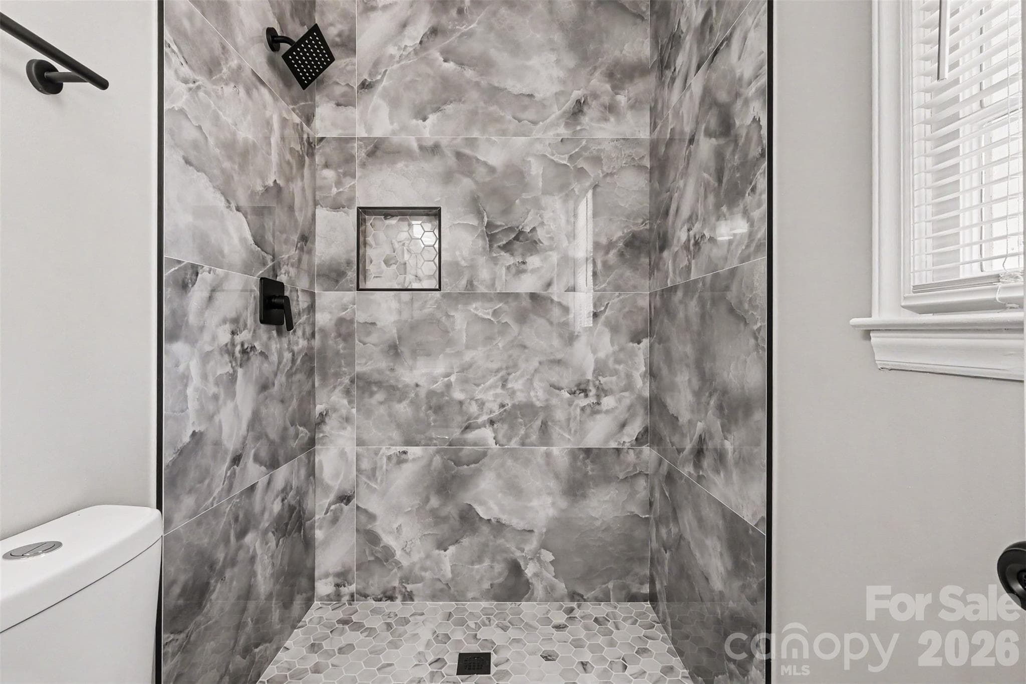 Custom walk-in shower featuring floor-to-ceiling dark porcelain tile, pebble tile flooring, matte black fixtures, and a bright window for natural light. - 3801 Hillock Court, Charlotte