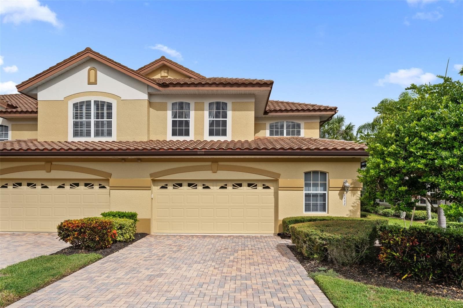 A paver driveway, tropical landscaping, and tile roof give this end-unit home inviting curb appeal. - 8432 MIRAMAR WAY, LAKEWOOD RANCH