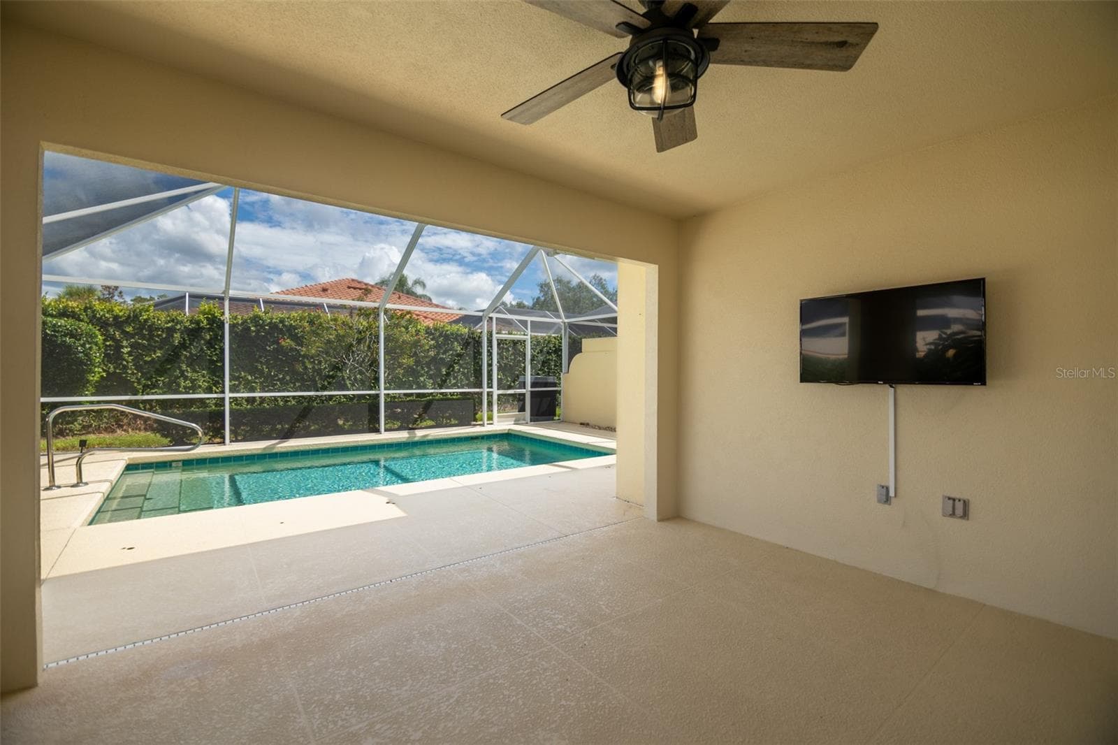 Back patio view of the pool in the center and wall mounted tv on the right. - 8876 ESTEPONA CT, SARASOTA