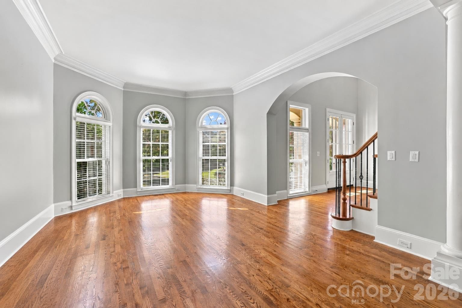 A large bay window with three arched windows brings plenty of natural light into this spacious living room, with hardwood floors and crown molding continuing the home’s classic architectural style. - 2309 Highland Forest Drive, Waxhaw