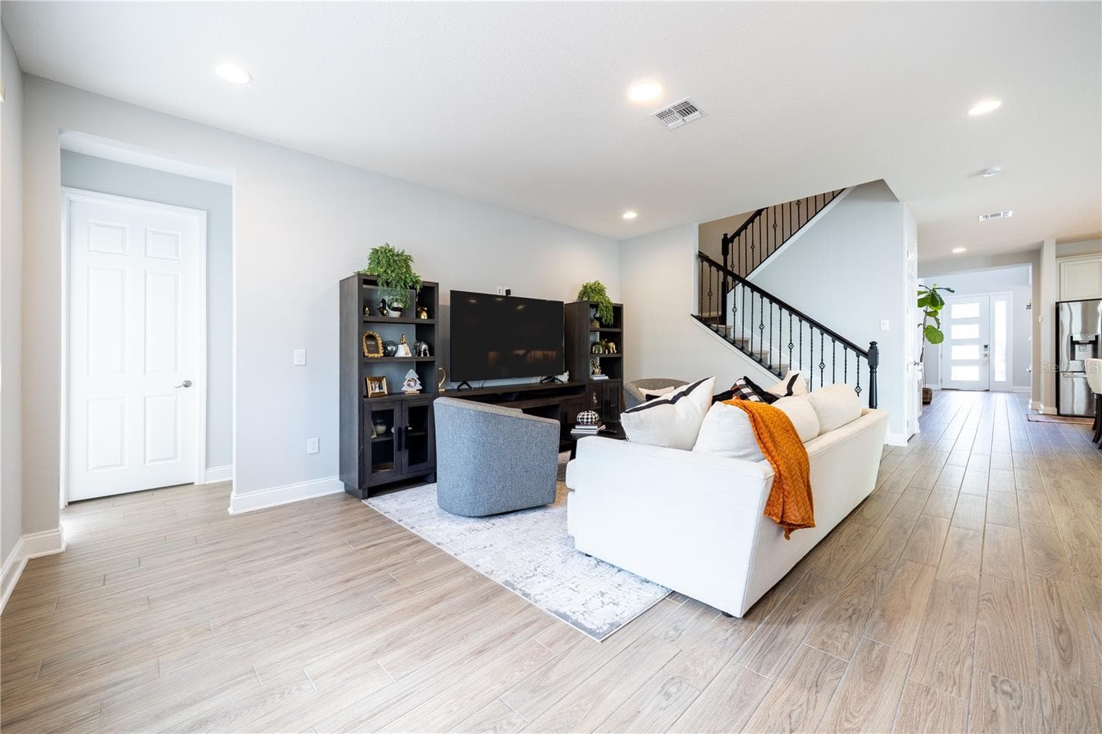 Open-concept living room with wood-look tile flooring and a staircase with decorative metal railings. - 1316 SOUTHERN SUN DRIVE, OAKLAND