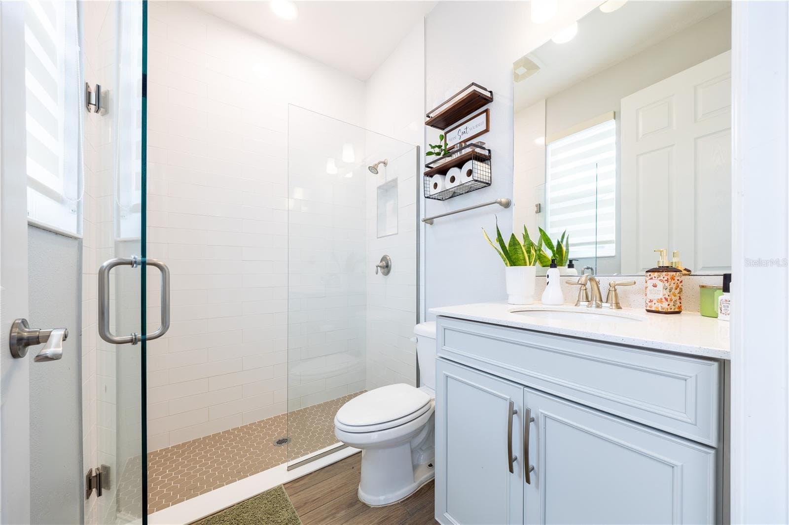 Bright bathroom with a frameless glass shower, white tile, mosaic shower floor, and light blue vanity. - 1316 SOUTHERN SUN DRIVE, OAKLAND
