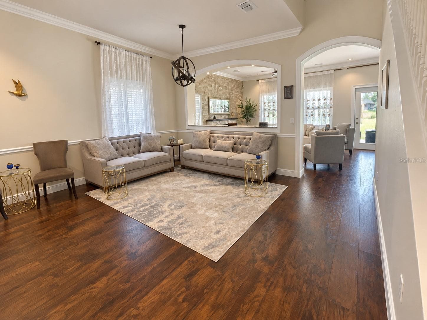 An airy sitting room near the entrance features crown molding, large windows, and an open connection to the formal dining area. Arched openings add character and connect the surrounding spaces. - 11117 ANCIENT FUTURES DR, TAMPA