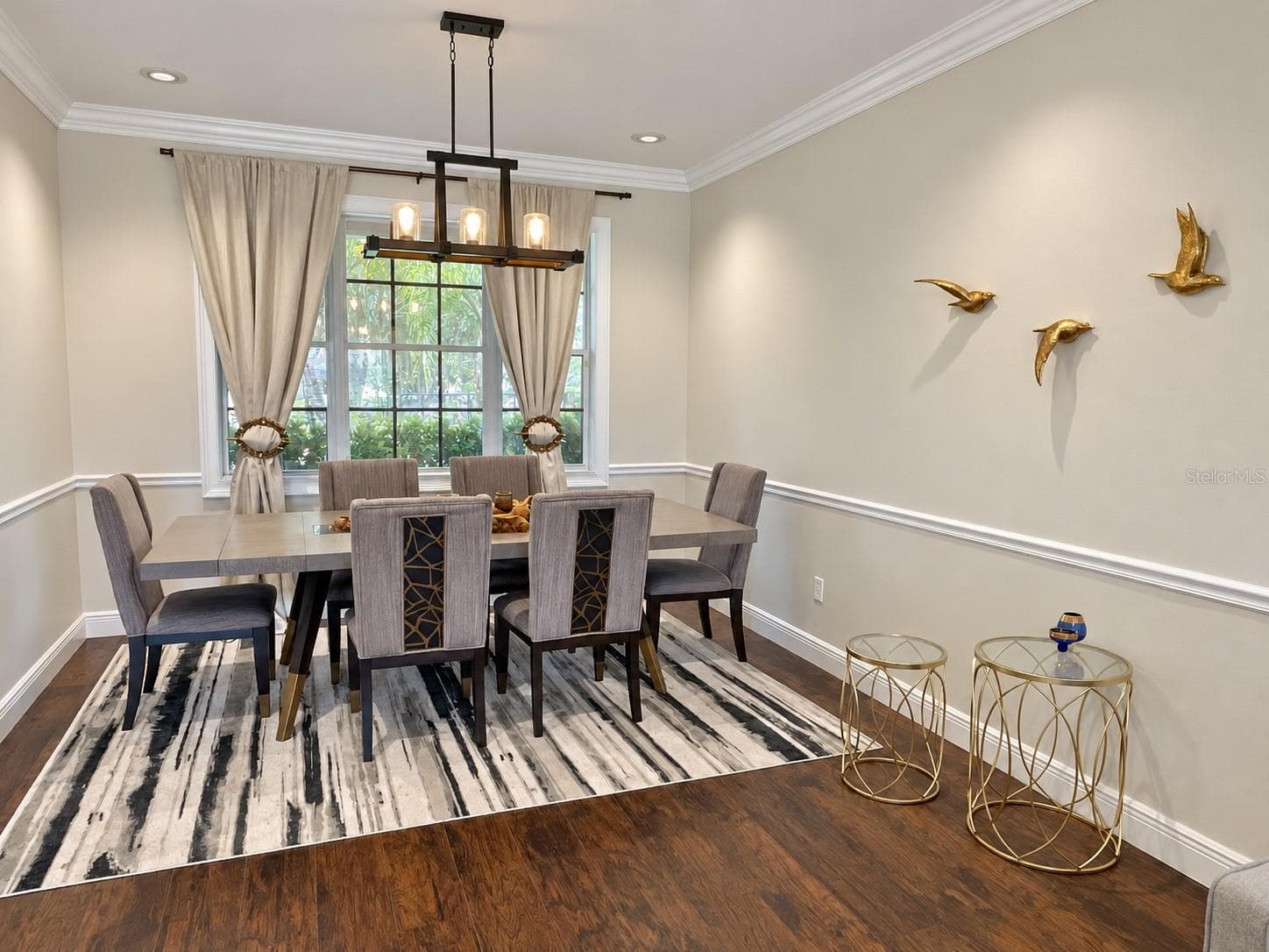 A dedicated dining area with a statement chandelier, chair-rail detailing, and crown molding. A large window adds natural light, and the adjoining living room creates a comfortable setting for entertaining. - 11117 ANCIENT FUTURES DR, TAMPA