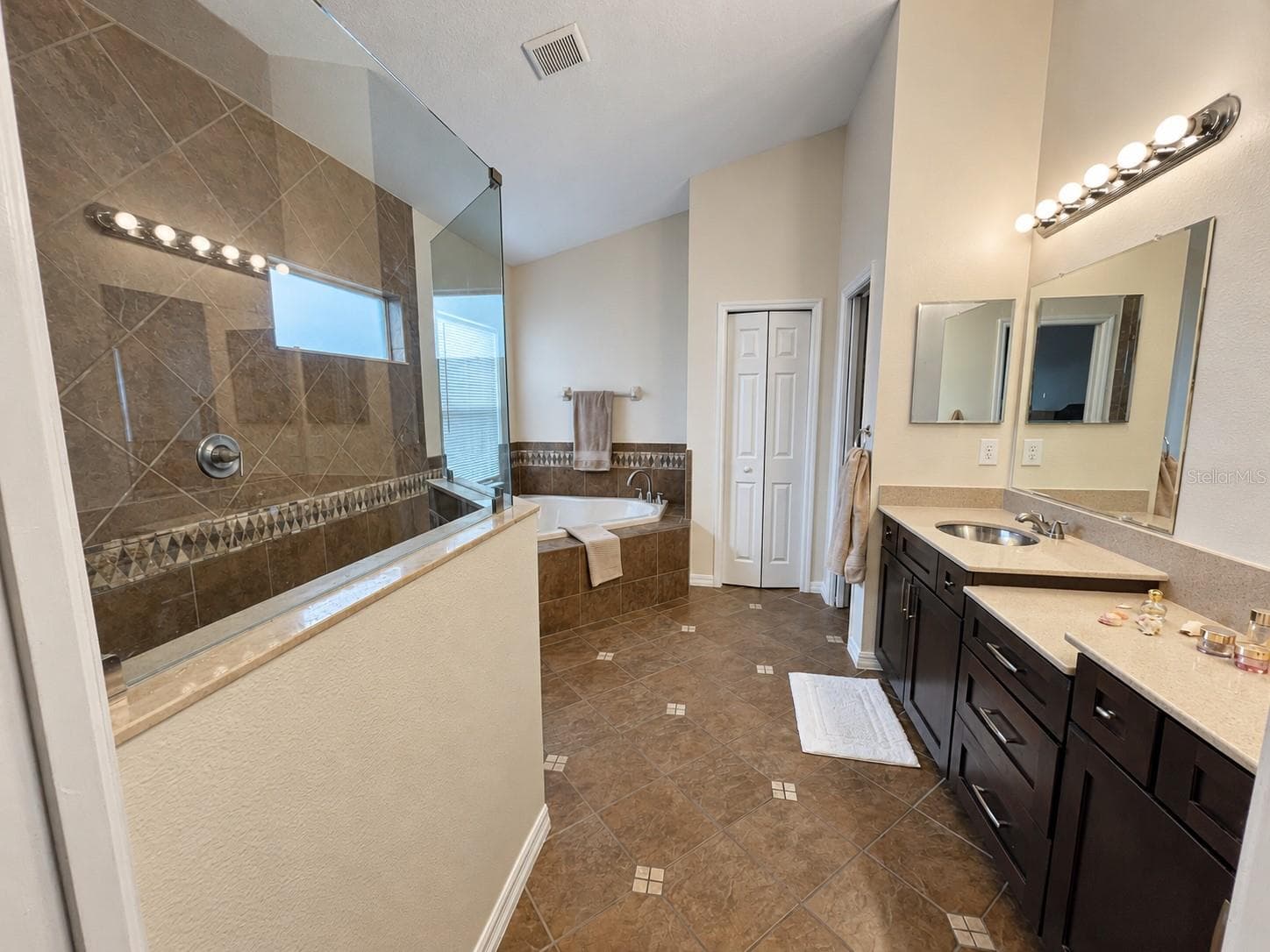 A generous bathroom featuring two sinks, extensive vanity storage, a separate soaking tub, and a walk-in shower with glass panels. High ceilings, natural light, and a separate toilet compartment enhance the layout. - 11117 ANCIENT FUTURES DR, TAMPA