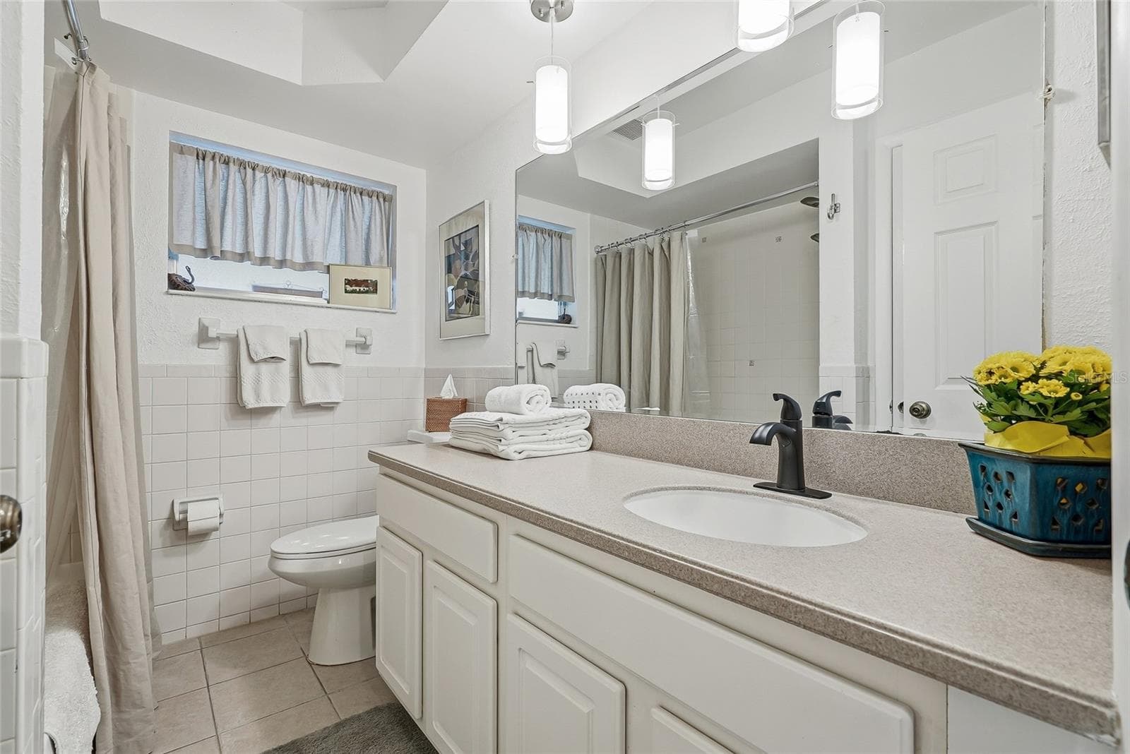 A generous vanity, broad mirror, and pendant lighting create a bright, comfortable space to get ready, with cabinet storage below. - 1890 62ND AVE S, ST PETERSBURG