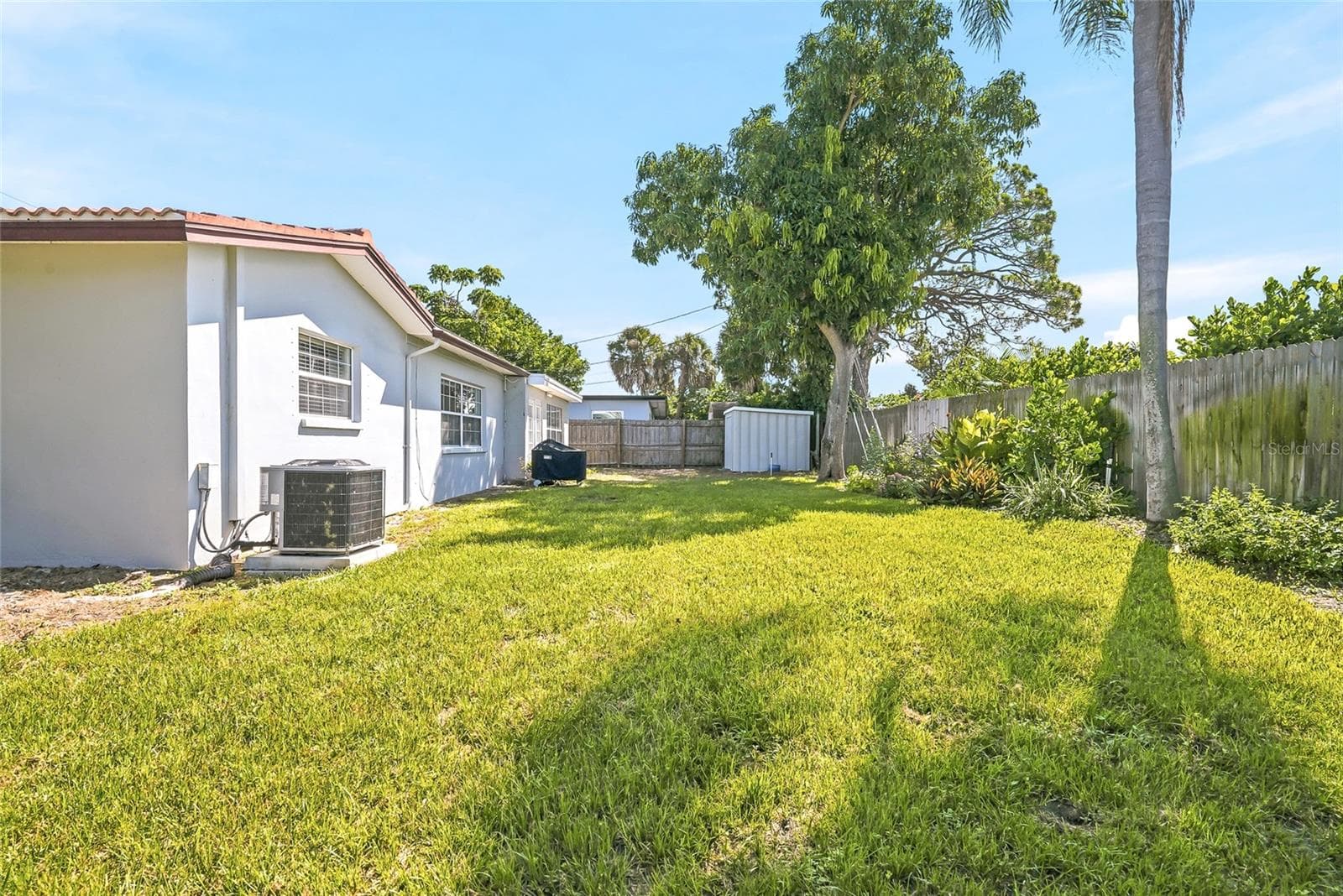 Stretch out in the sunshine or settle beneath the trees, with open lawn, established planting beds, and wood fencing framing the backyard. - 1890 62ND AVE S, ST PETERSBURG