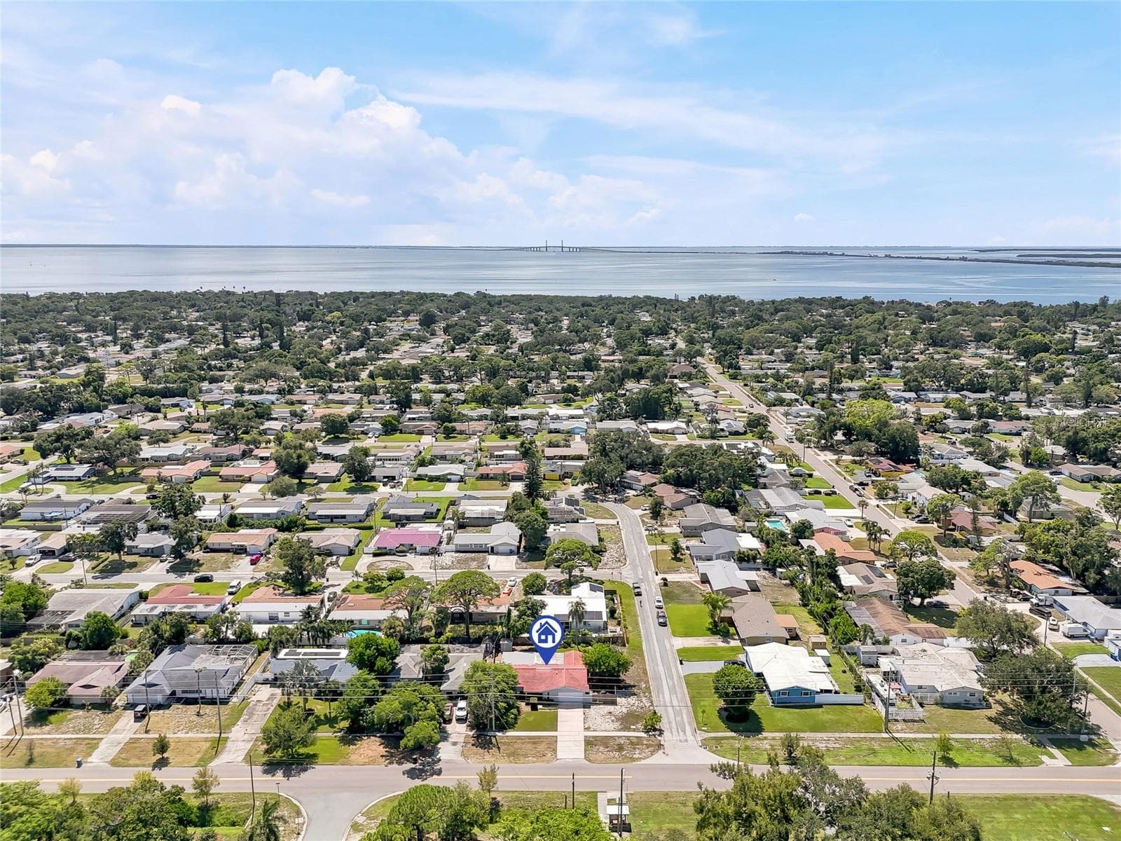A wider aerial perspective places the home within its leafy St. Petersburg neighborhood, with the bay and Sunshine Skyway Bridge on the horizon. - 1890 62ND AVE S, ST PETERSBURG