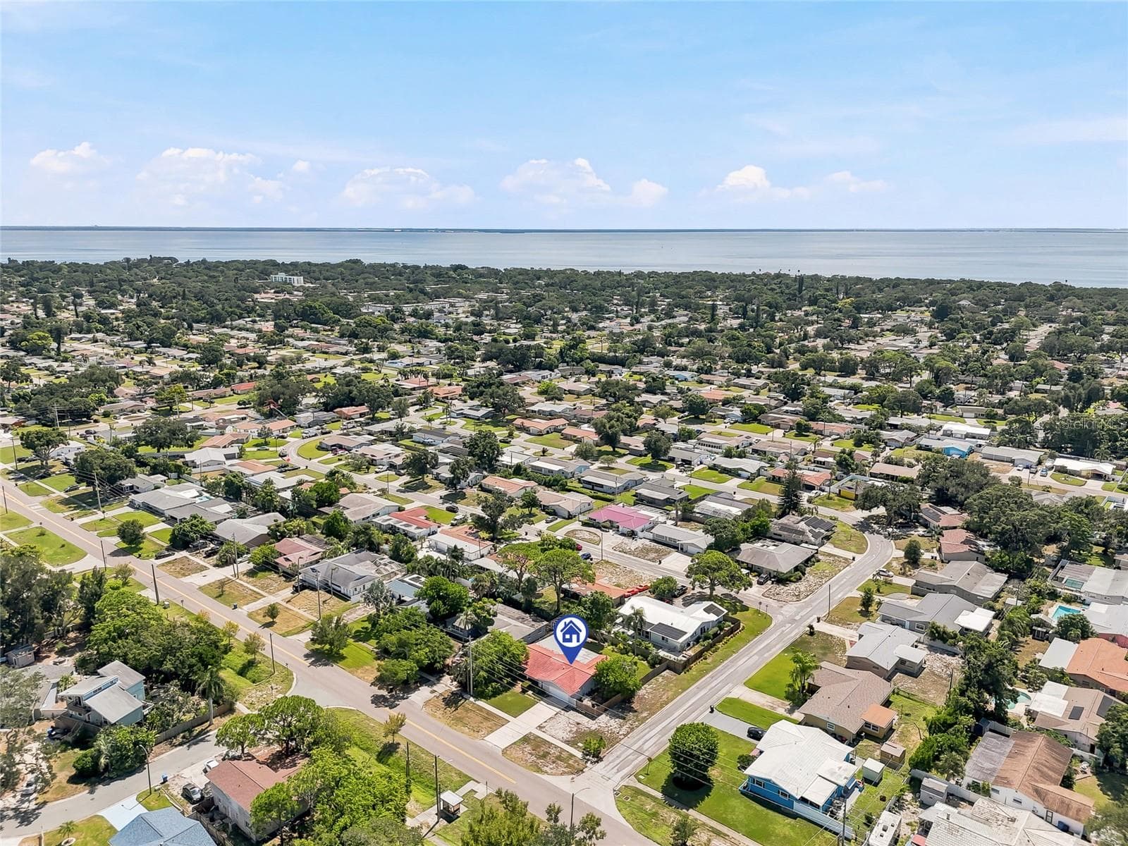 An elevated view highlights the home’s corner lot and tree-filled surroundings, with the bay forming a scenic backdrop beyond the neighborhood. - 1890 62ND AVE S, ST PETERSBURG