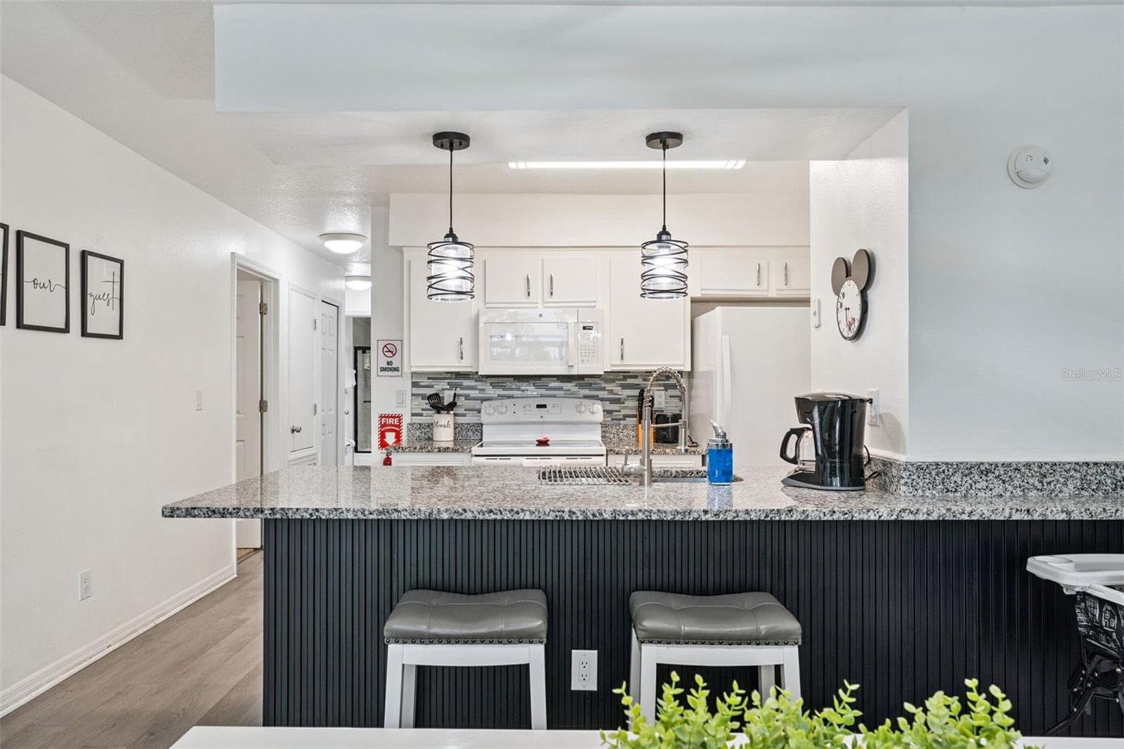 Breakfast Bar Seating: Custom vertical-slat accent breakfast bar with granite countertop overhang, stool seating, and updated pendant light fixtures. - 5017 LAGUNA BAY CIR #100, KISSIMMEE