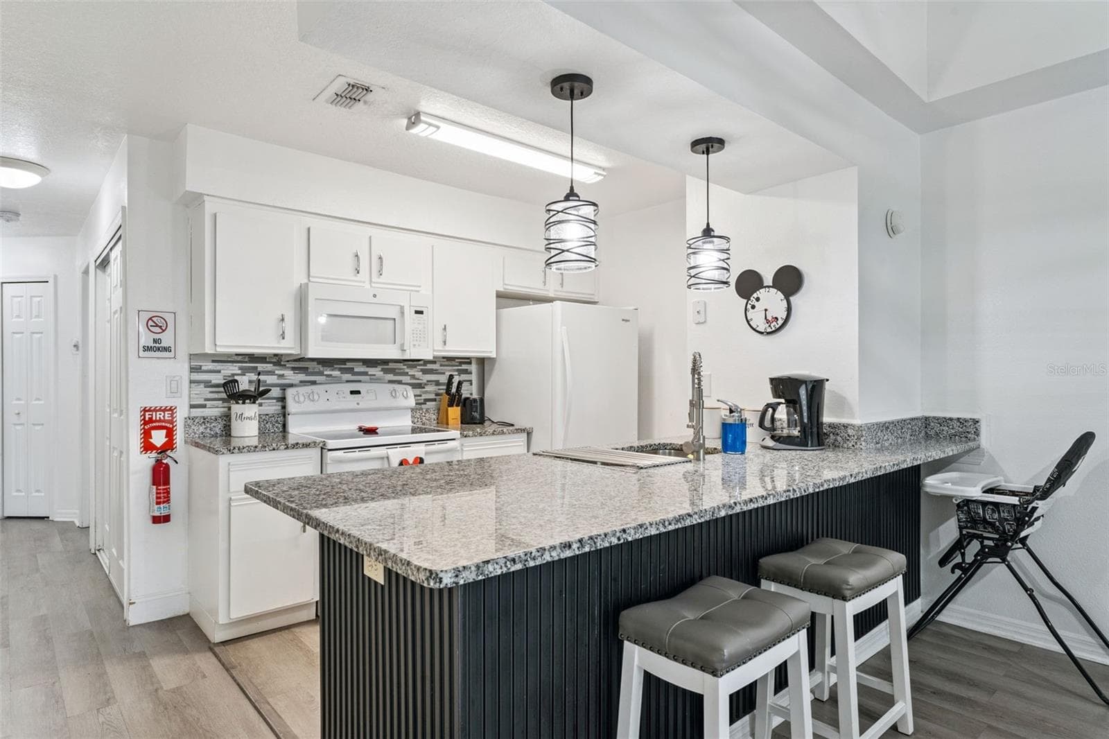 Kitchen Island & Bar: Alternate angle of the kitchen peninsula bar with seating, rich dark wood-paneling detail, and view into the full kitchen suite. - 5017 LAGUNA BAY CIR #100, KISSIMMEE