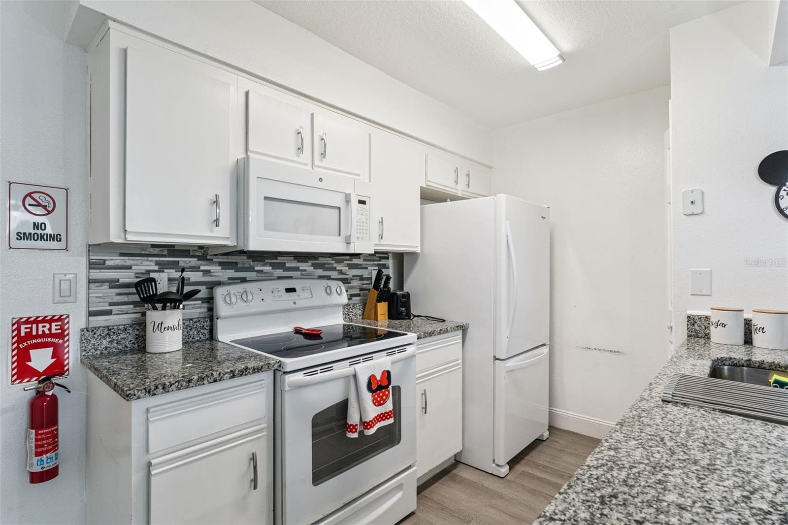 Kitchen Interior: Bright kitchen equipped with clean white cabinetry, granite countertops, a mosaic tile backsplash, electric range, and matching white appliances. - 5017 LAGUNA BAY CIR #100, KISSIMMEE
