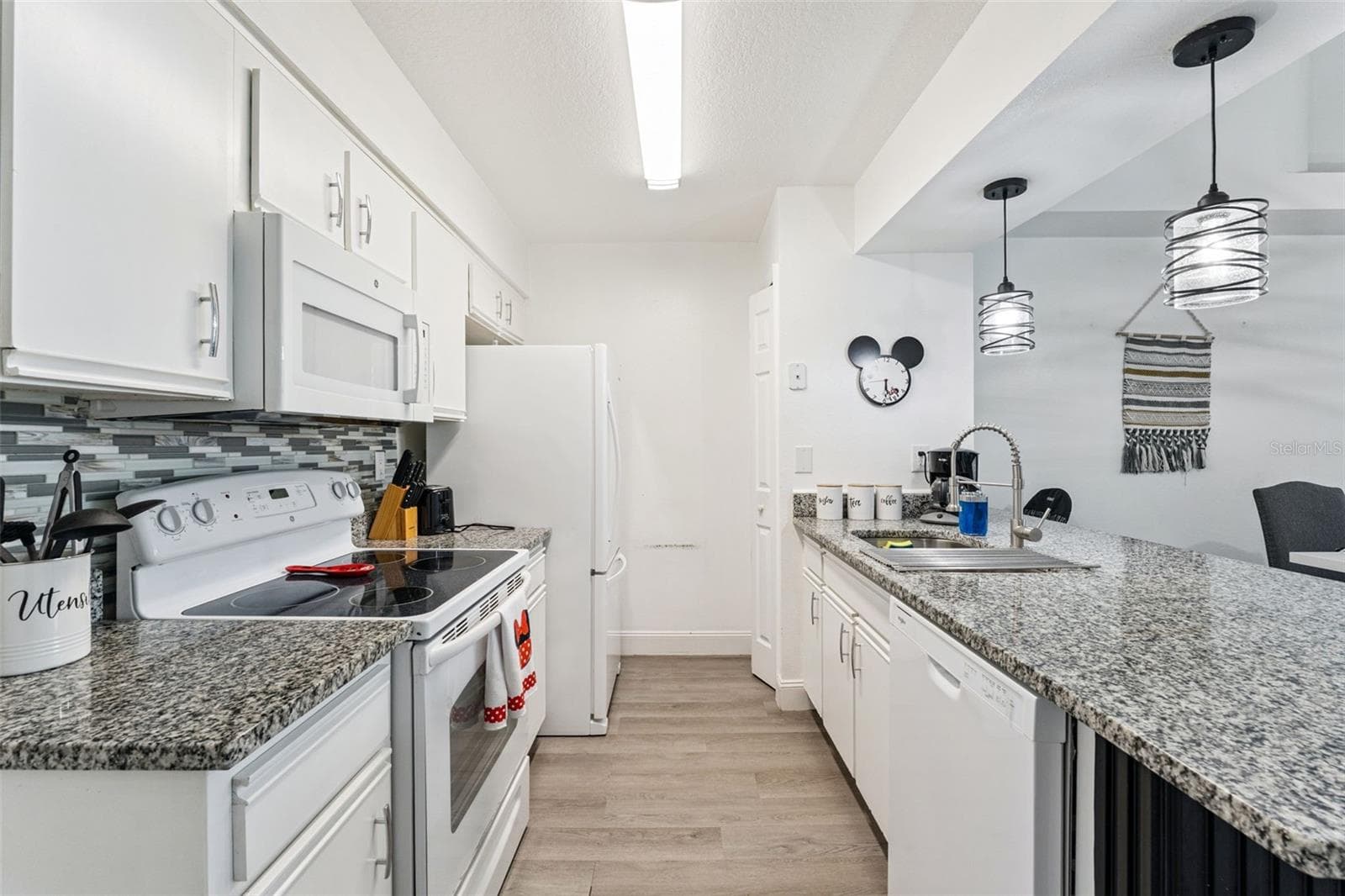 Kitchen & Breakfast Bar: Kitchen perspective highlighting durable granite counters, undermount sink with goose-neck faucet, dishwasher, and modern pendant lights over the peninsula. - 5017 LAGUNA BAY CIR #100, KISSIMMEE