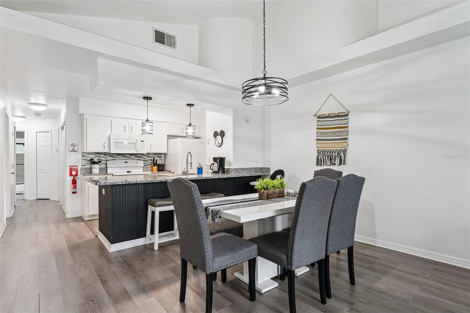 Dining & Kitchen Flow: View of the dining area looking into the open kitchen, featuring high ceilings, modern pendant lighting, wood-look plank flooring, and a sleek breakfast bar. - 5017 LAGUNA BAY CIR #100, KISSIMMEE