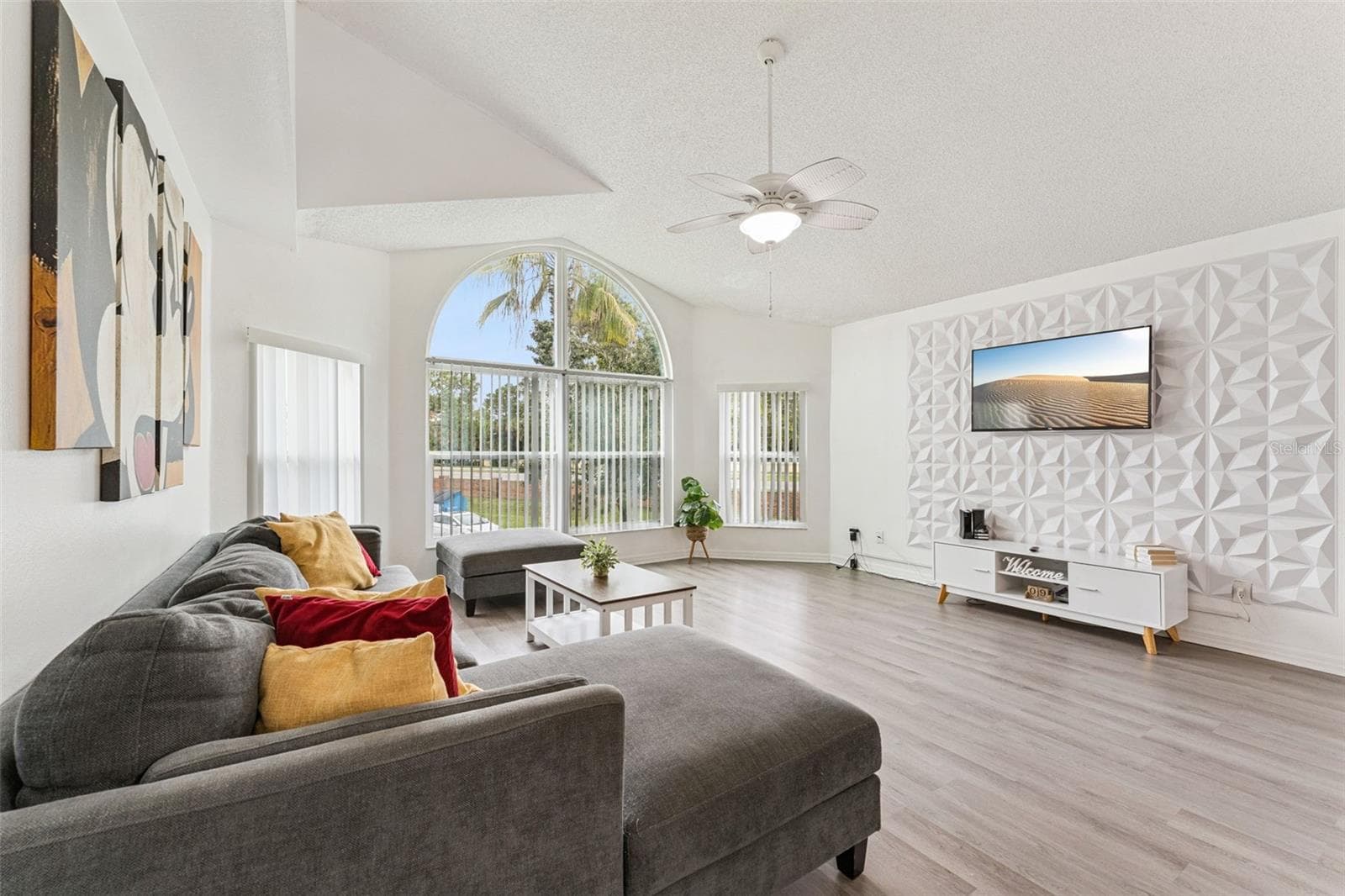 Living Room Alternate View: View of the main living area showcasing the custom 3D accent wall, media console, wall-mounted TV, and spacious layout. - 5017 LAGUNA BAY CIR #100, KISSIMMEE