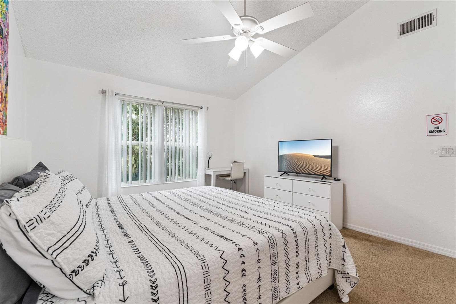 Primary Bedroom: Bright primary bedroom featuring vaulted ceilings, a ceiling fan, plush carpeting, dedicated work/desk nook, and large window for natural light. - 5017 LAGUNA BAY CIR #100, KISSIMMEE