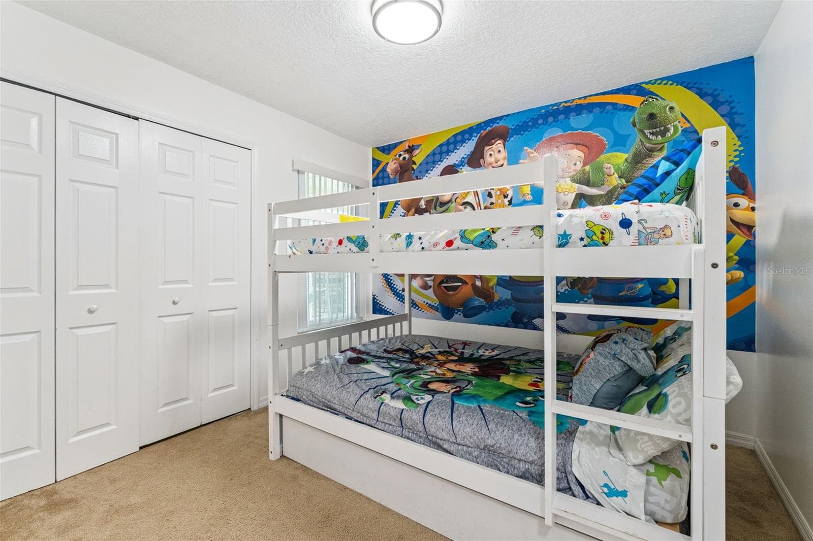 Character Bunk Room View: Alternate angle of the bunk bedroom showcasing double bi-fold closet doors and colorful themed wall graphics - 5017 LAGUNA BAY CIR #100, KISSIMMEE