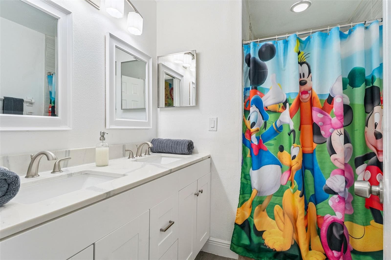 Guest Bathroom Double Vanity: Guest bathroom featuring a crisp white vanity, modern stone-look countertop, dual sinks, and framed mirrors. - 5017 LAGUNA BAY CIR #100, KISSIMMEE