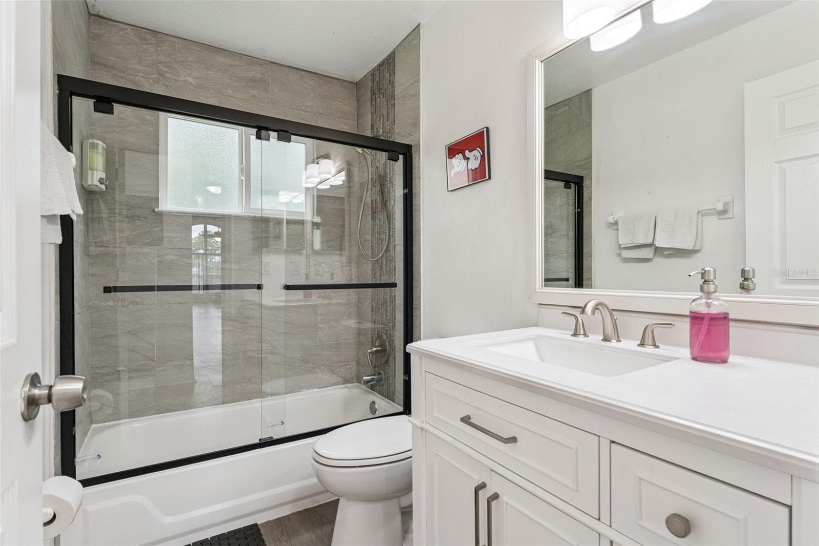 Full Bathroom & Shower: Updated full bathroom complete with a white vanity, modern matte black sliding glass shower doors, and sleek tile surround. - 5017 LAGUNA BAY CIR #100, KISSIMMEE