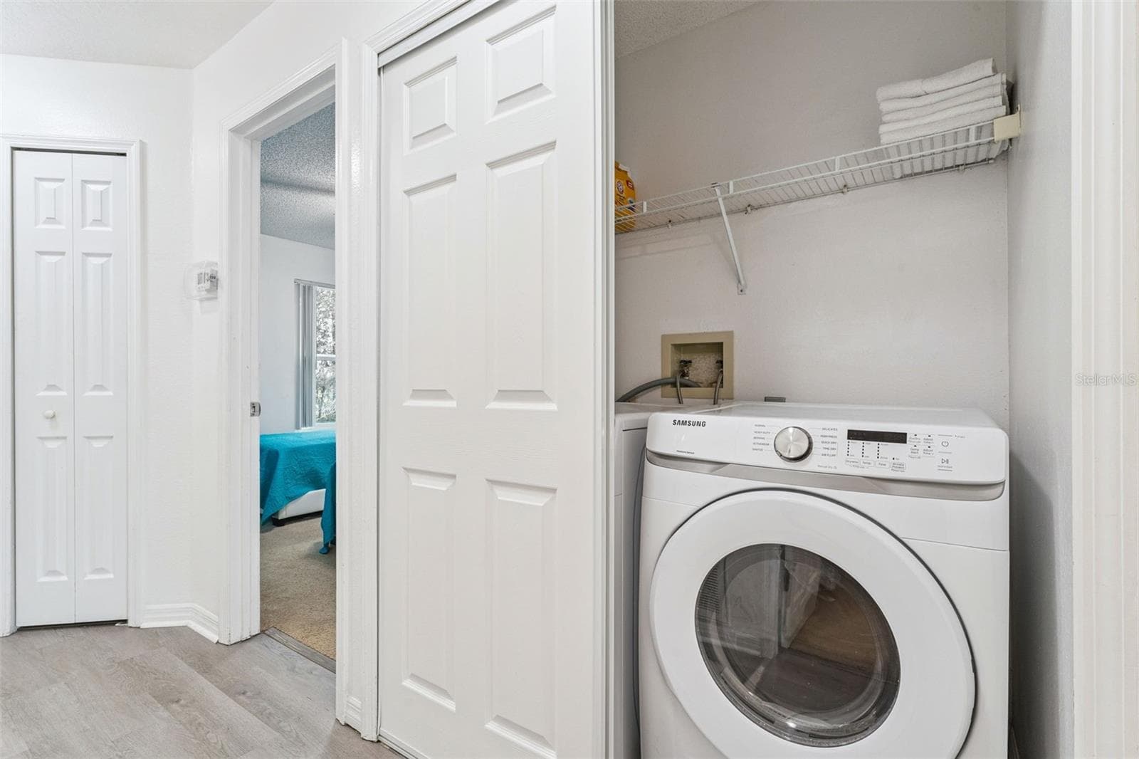 In-Unit Laundry Closet: Convenient in-unit laundry closet featuring a front-loading Samsung washer and built-in wire storage shelving - 5017 LAGUNA BAY CIR #100, KISSIMMEE