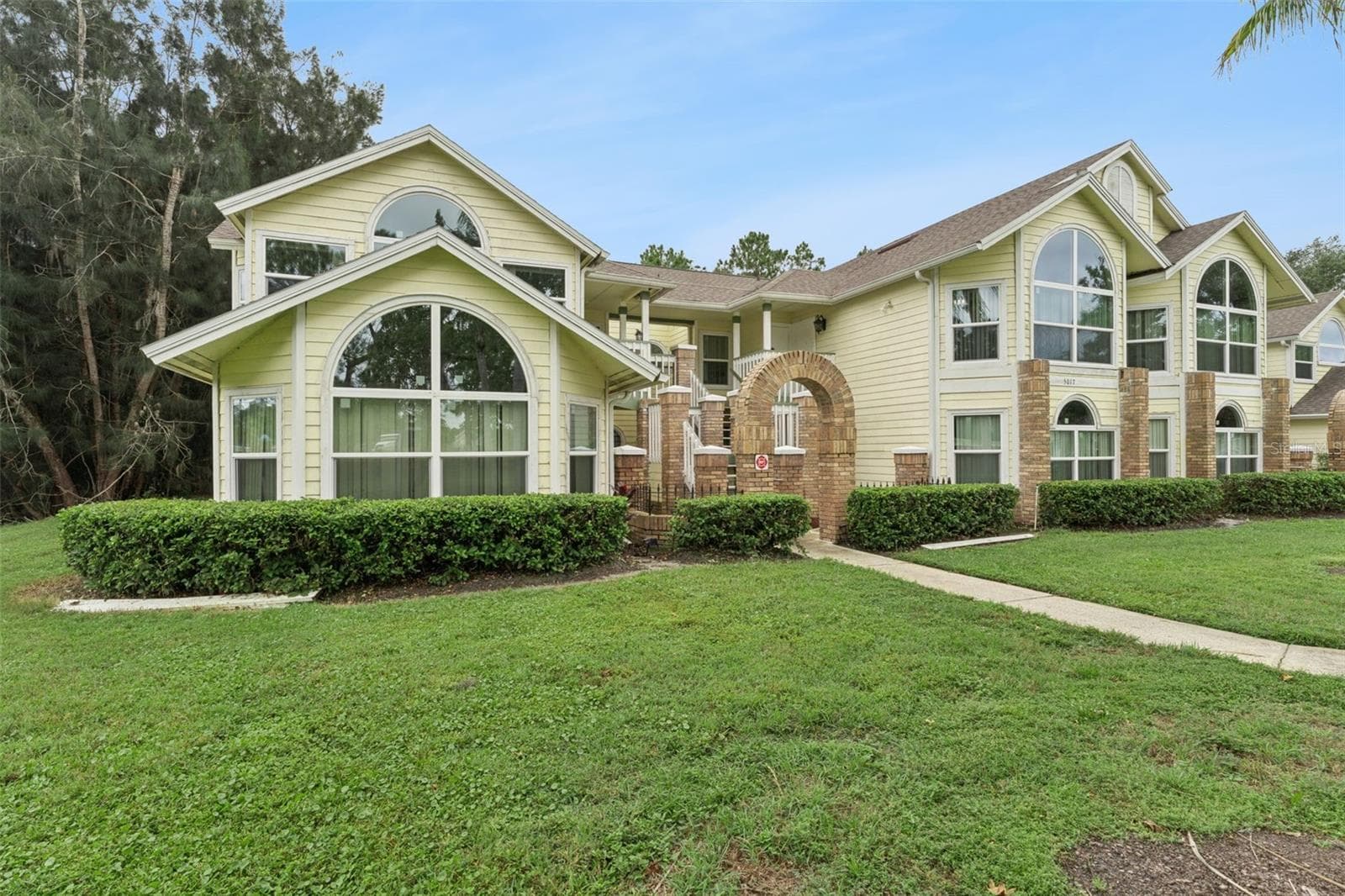 Exterior Side View: Angled building view highlighting grand arched windows, brick accents, low-maintenance hedge landscaping, and lush lawn. - 5017 LAGUNA BAY CIR #100, KISSIMMEE