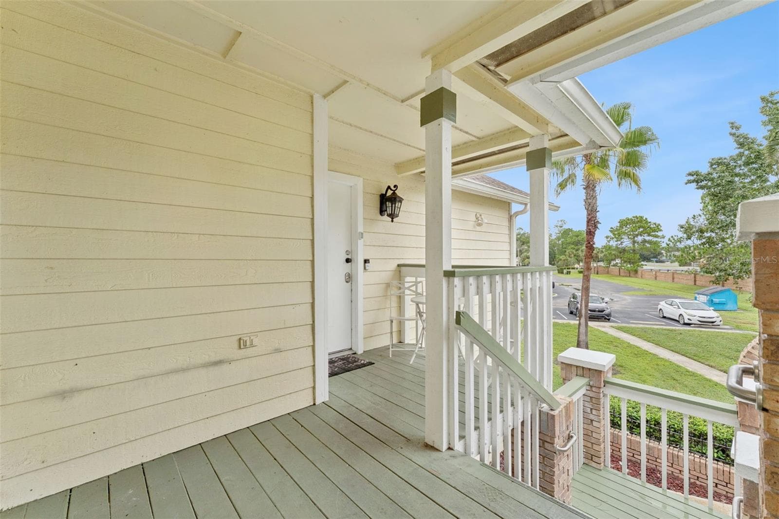 Covered Entry Deck: Covered front porch featuring painted wood decking, classic railing, brick column accents, and entry lighting - 5017 LAGUNA BAY CIR #100, KISSIMMEE