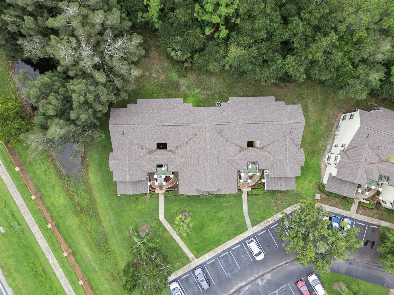 Top-Down Aerial View: Direct overhead drone perspective highlighting the building roofline, front entryway paths, and mature tree borders - 5017 LAGUNA BAY CIR #100, KISSIMMEE