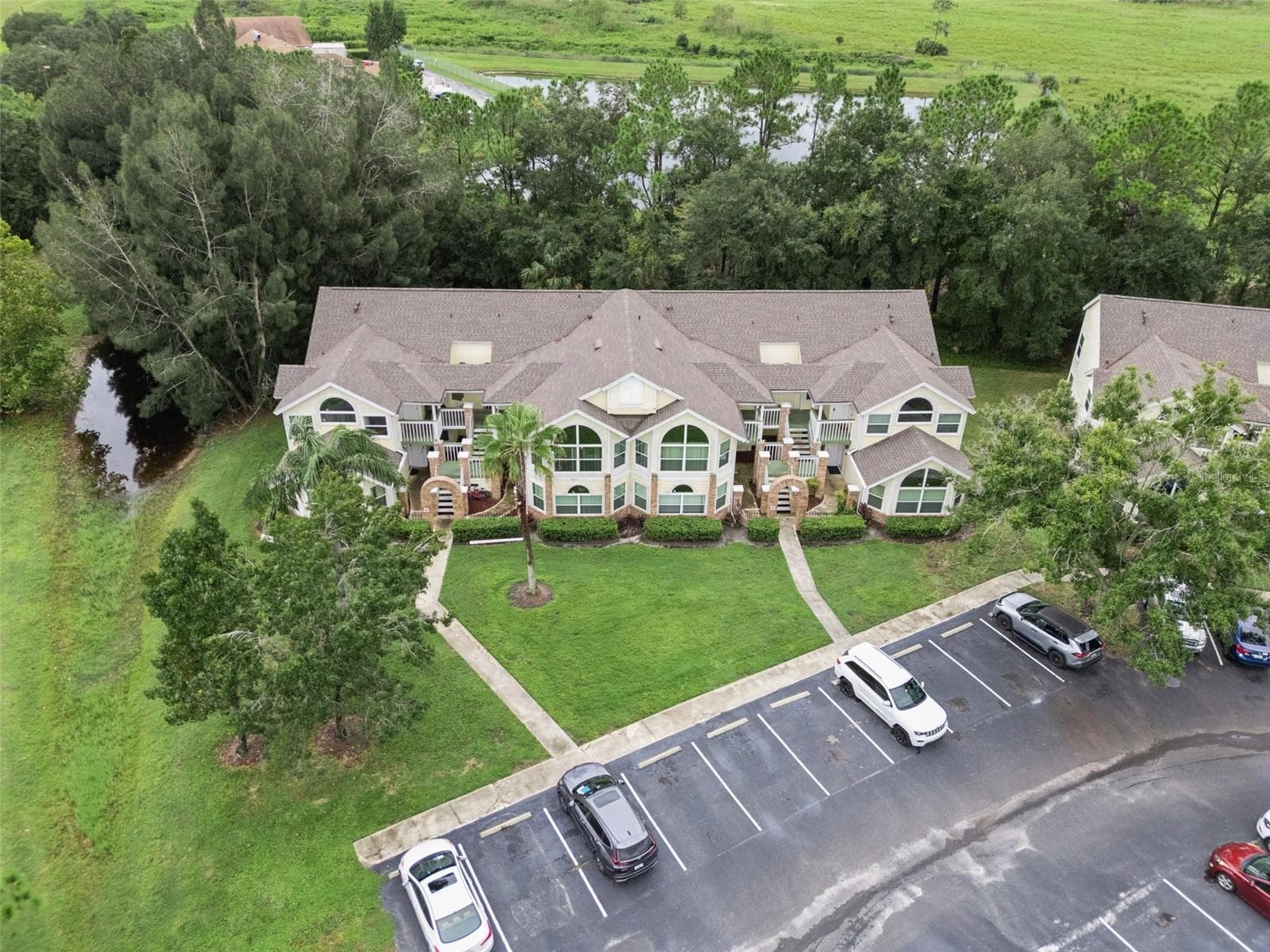 Building Aerial Overview: Elevated drone shot showing the front building elevation, manicured lawn, and convenient resident parking spaces - 5017 LAGUNA BAY CIR #100, KISSIMMEE