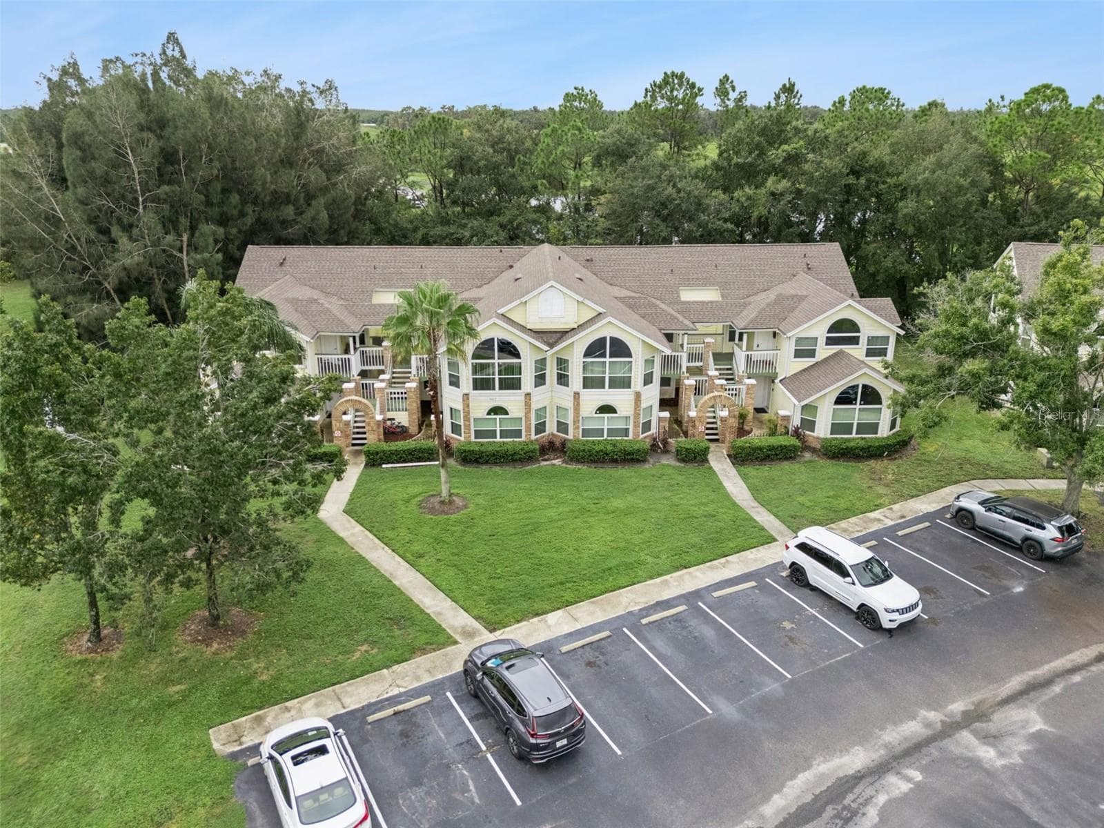 Exterior Aerial Perspective: Front aerial view displaying the building facade, brick architectural entries, central palm landscaping, and parking lot - 5017 LAGUNA BAY CIR #100, KISSIMMEE