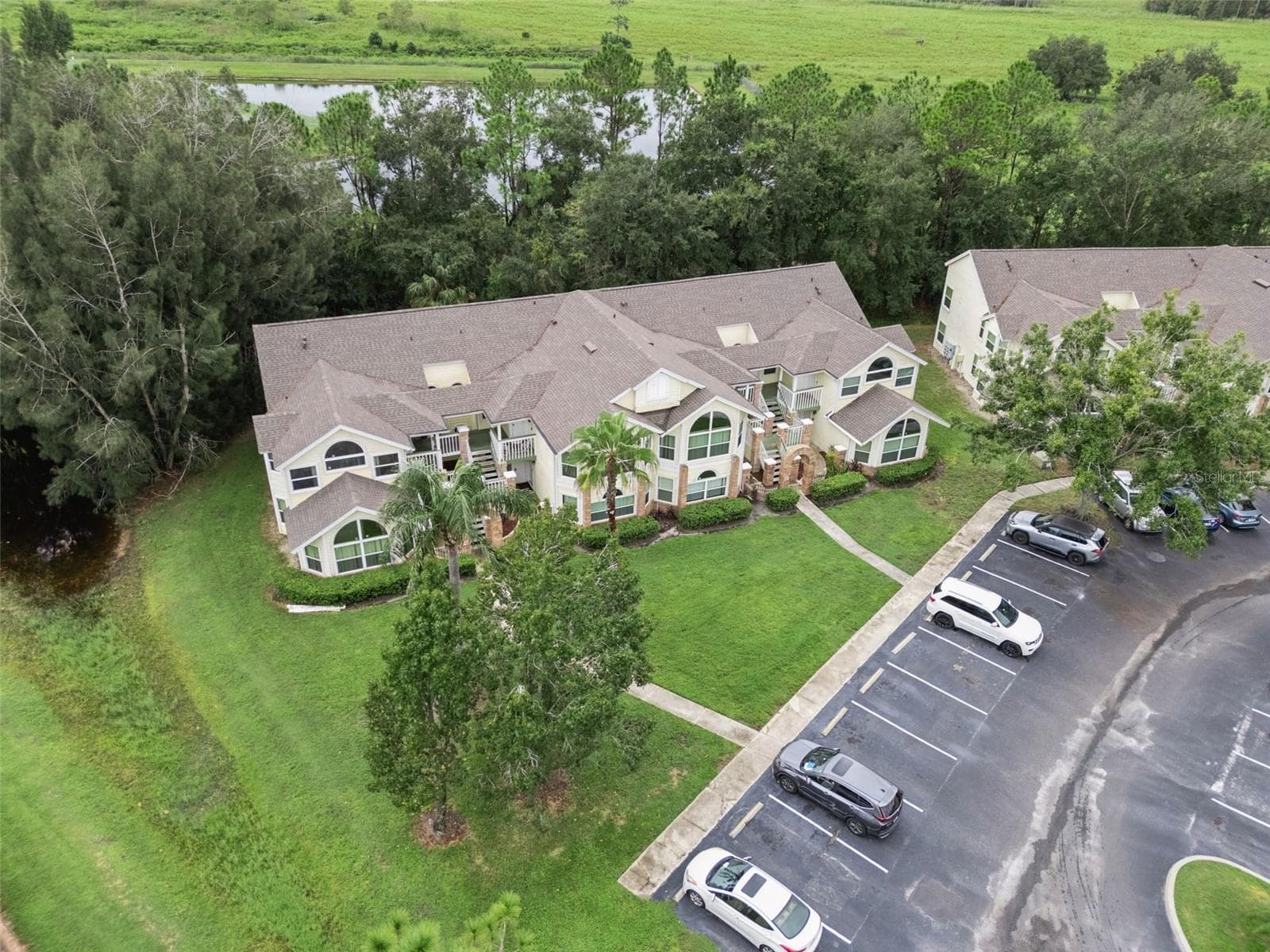 Aerial Setting & Conservation View: High-angle aerial view showcasing the building tucked alongside a peaceful water feature and lush wooded backdrop - 5017 LAGUNA BAY CIR #100, KISSIMMEE