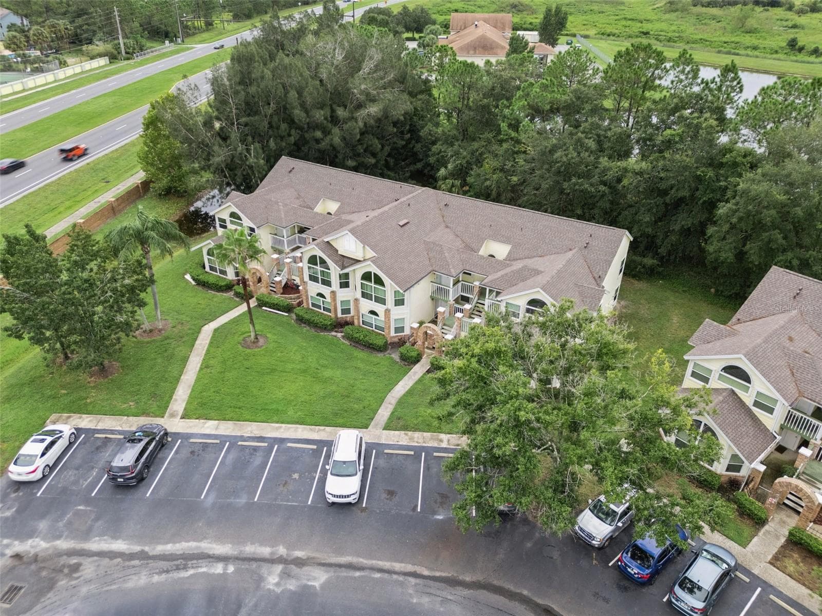Front Aerial & Parking: High-angle front aerial view of the building, highlighting convenient front parking stalls, paved walkways, and lush surrounding greenery. - 5017 LAGUNA BAY CIR #100, KISSIMMEE