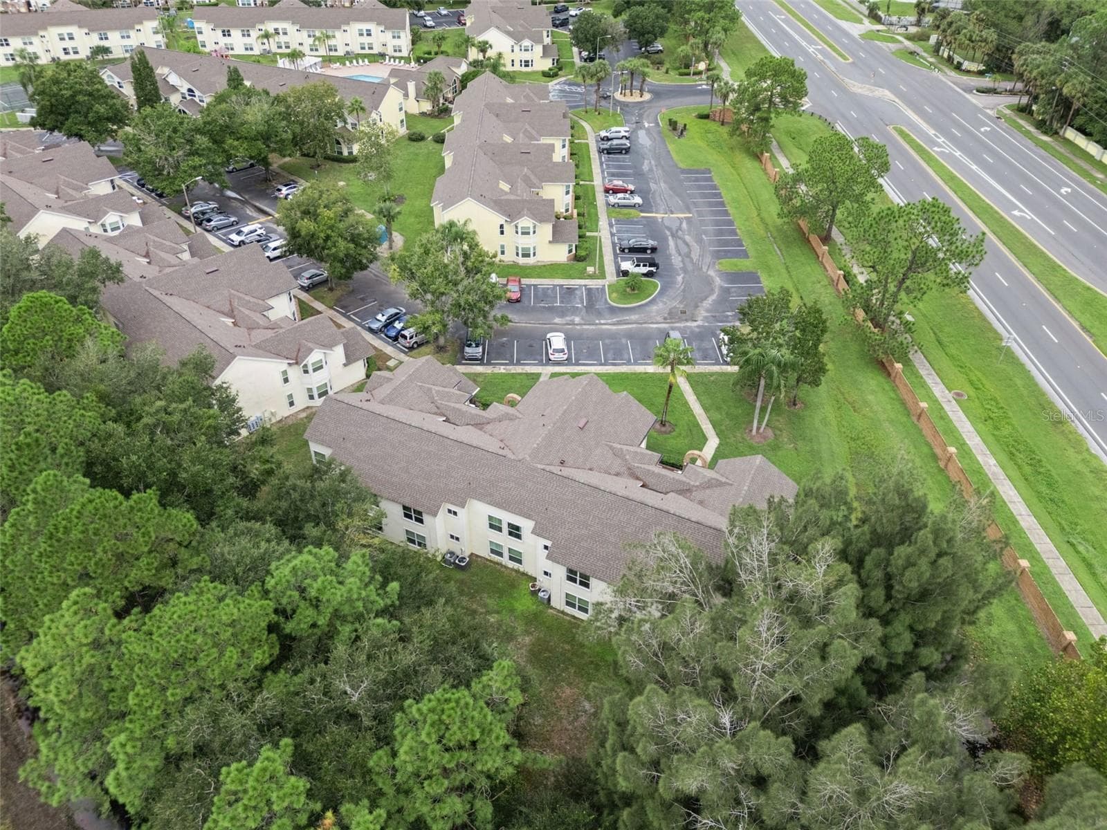 Rear Exterior Aerial: Overhead aerial perspective of the building's rear, showing rooflines, bordering pine tree conservation area, and neighborhood surroundings - 5017 LAGUNA BAY CIR #100, KISSIMMEE
