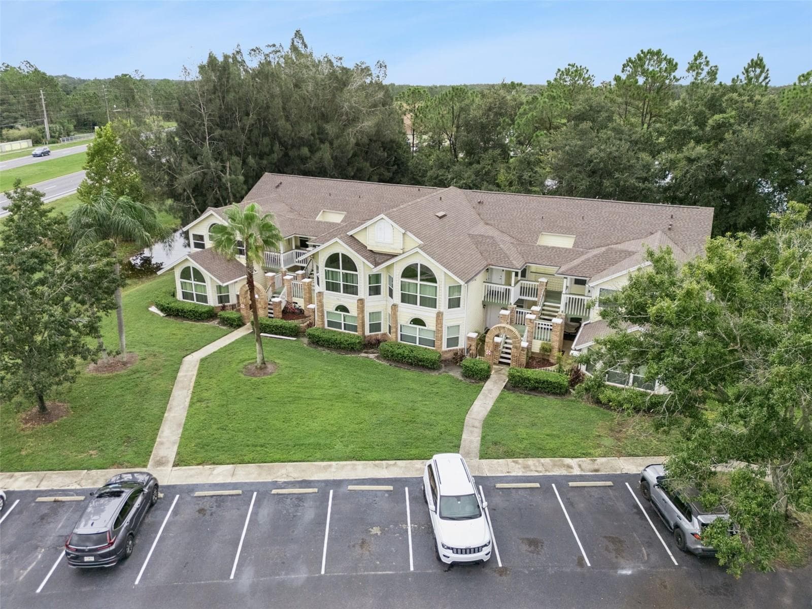 Building Facade Aerial: Focused front aerial capture highlighting the exterior facade, brick-accented entryways, central lawn, and parking access. - 5017 LAGUNA BAY CIR #100, KISSIMMEE